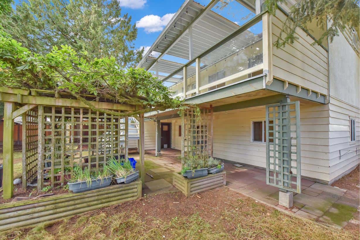 Spacious backyard of a modern family home with a raised deck, outdoor patio area, garden beds, and lush greenery, ideal for outdoor living and summer gatherings.