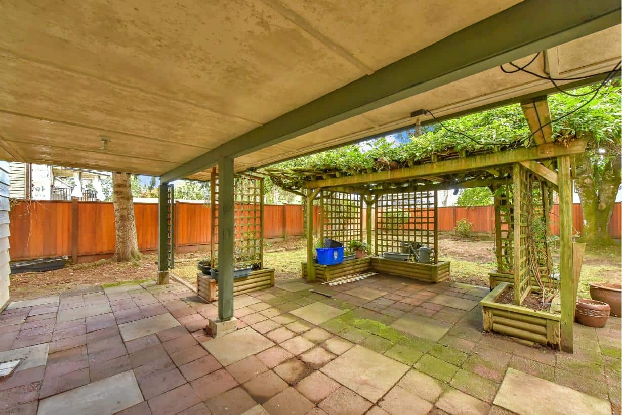 Fenced backyard patio with wooden pergola, garden beds, and mature trees, ideal for outdoor living and entertaining in Victoria, Vancouver Island.
