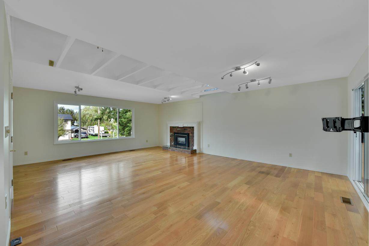 Spacious living room with hardwood floors and a fireplace, ideal for Vancouver Island real estate listings. Modern interior with large windows and abundant natural light.