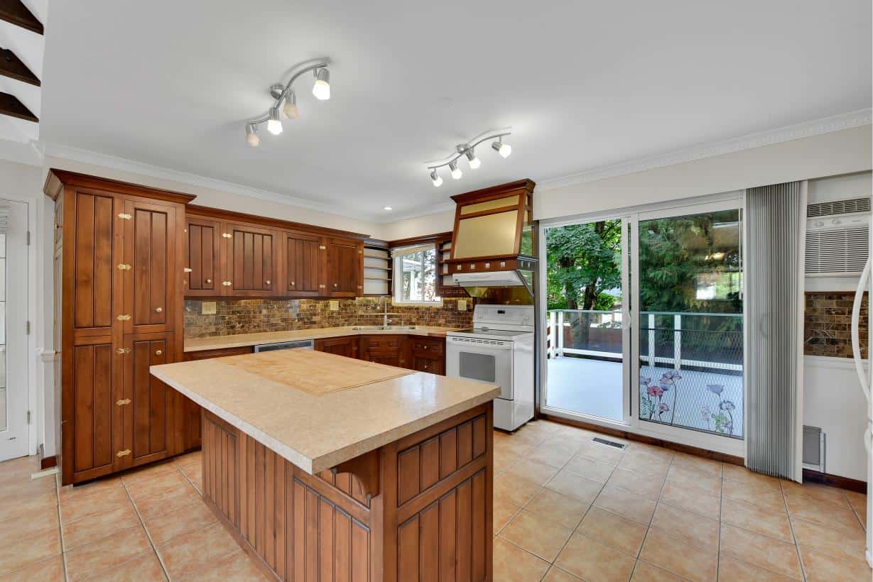 Modern kitchen with wooden cabinetry, brick backsplash, and stainless steel appliances, opening to a balcony with lush greenery, perfect for Toronto real estate buyers seeking spacious and updated homes.