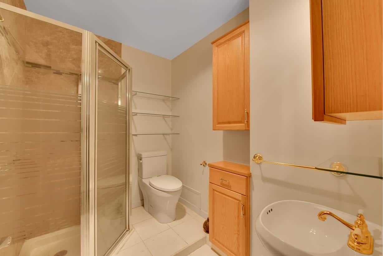 Clean modern bathroom with glass shower, wooden cabinetry, and white fixtures, perfect for easier living and storage in Vancouver real estate.