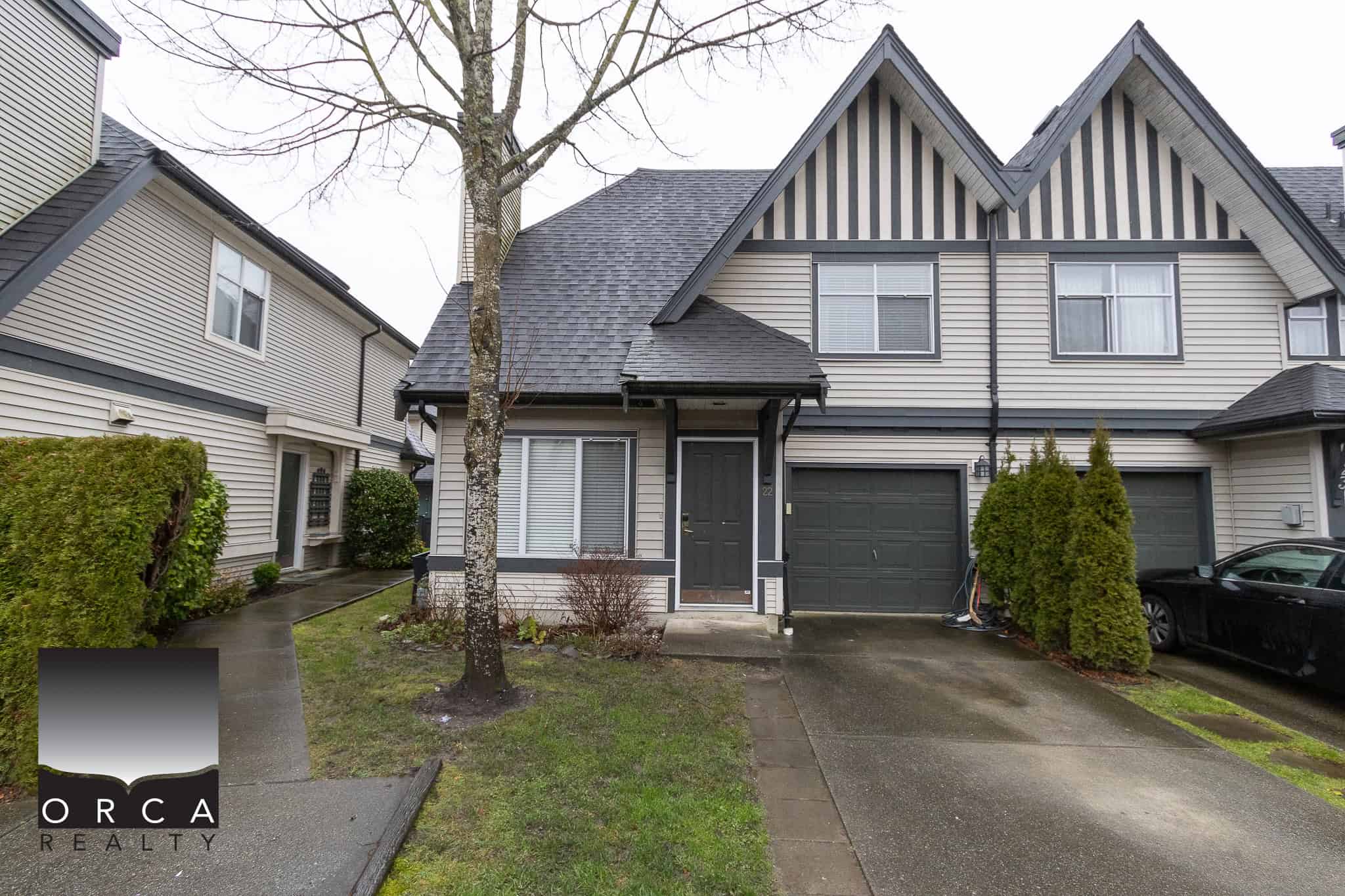 Spacious townhouse with modern exterior, attached garage, front yard, and lush landscaping, ideal for Vancouver housing market, offered by Orca Realty Inc. in BC.