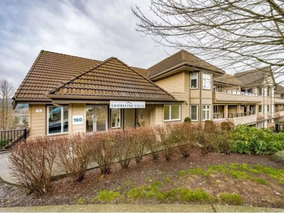 Charming Shoreline Villa apartment complex with beige siding, brown tile roofs, and spacious balconies located in a scenic area with landscaped gardens and leafless trees.