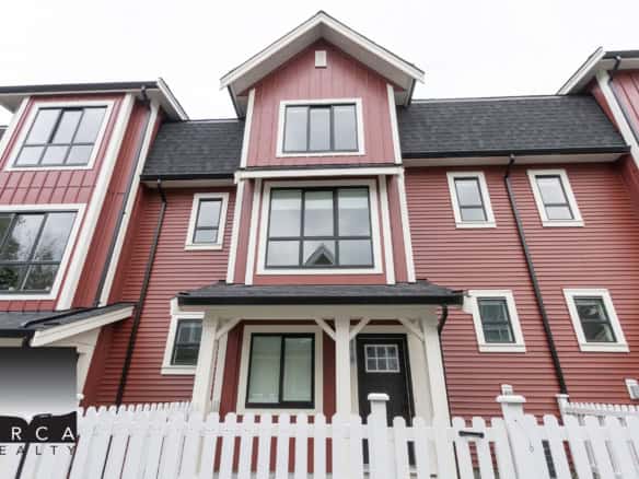 Bright red modern townhouse with white trim, multiple large windows, and a white picket fence, ideal for family living in the Vancouver real estate market.