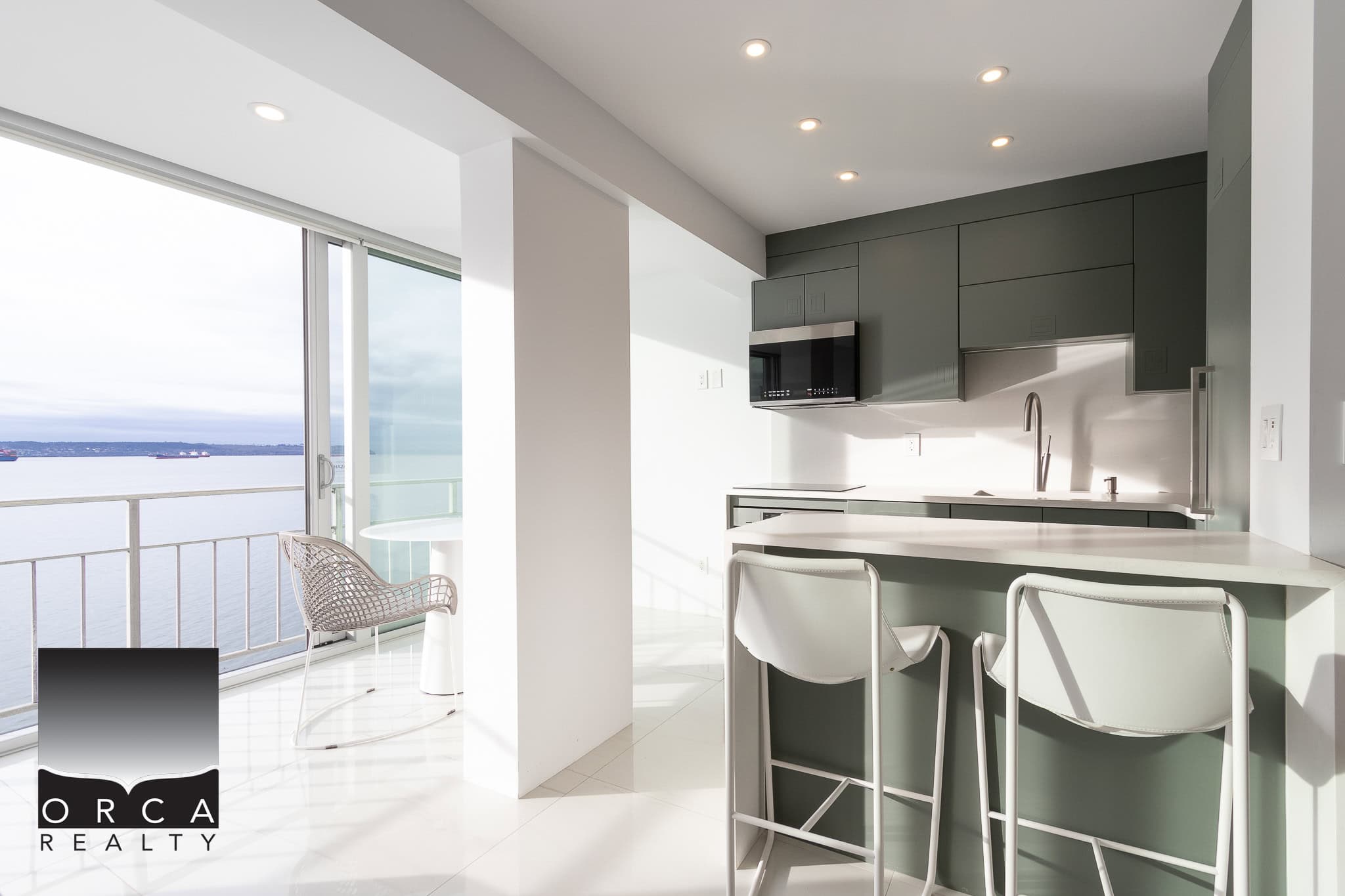 Stunning modern kitchen with ocean view, featuring sleek grey cabinetry, minimalist design, and a spacious breakfast bar in a waterfront condo by Orca Realty Inc.