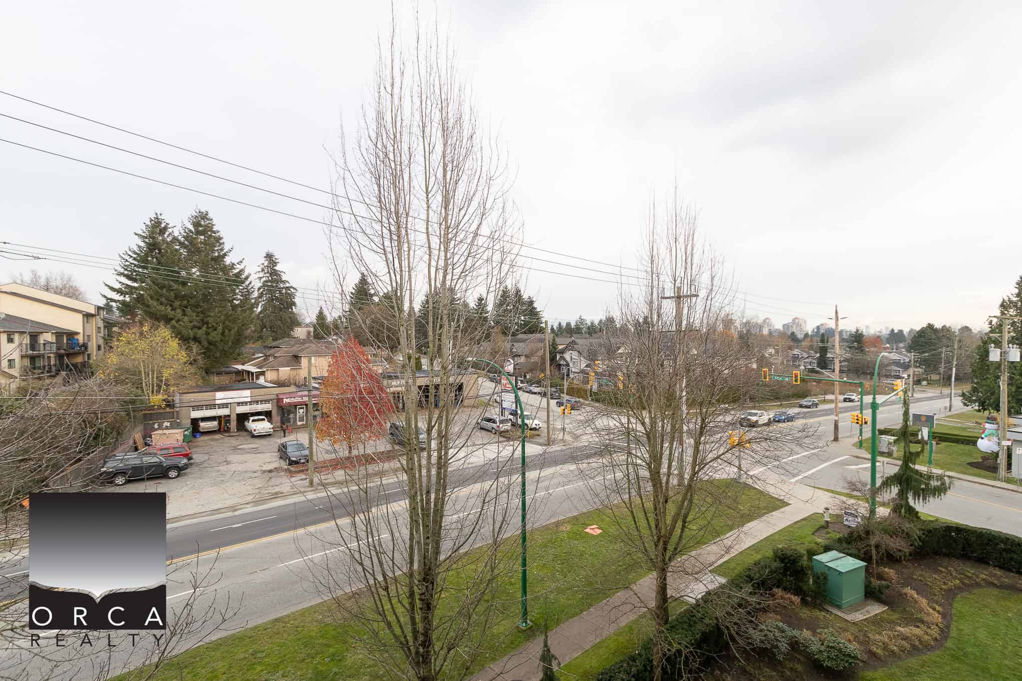 Vibrant neighbourhood street view with commercial buildings, parked cars, and mature trees, showcasing the community vibe and accessibility near Orca Realty Inc. in BC.