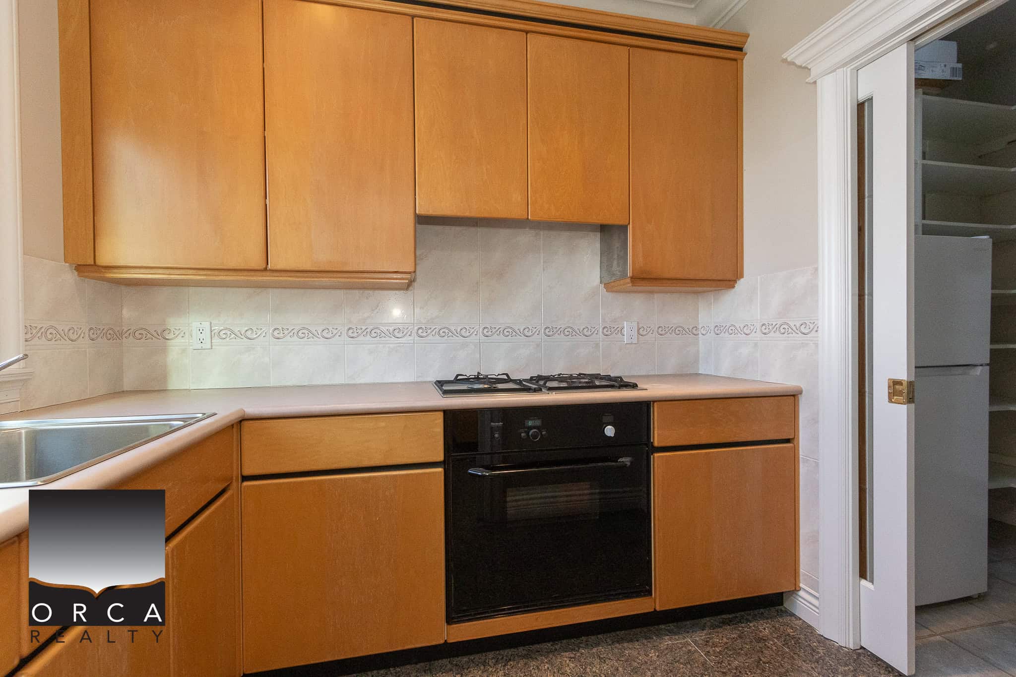 12 Bright kitchen with wooden cabinets, black oven, gas stovetop, tiled backsplash, and adjacent pantry in a Vancouver-area home. Perfect for modern living and entertaining.