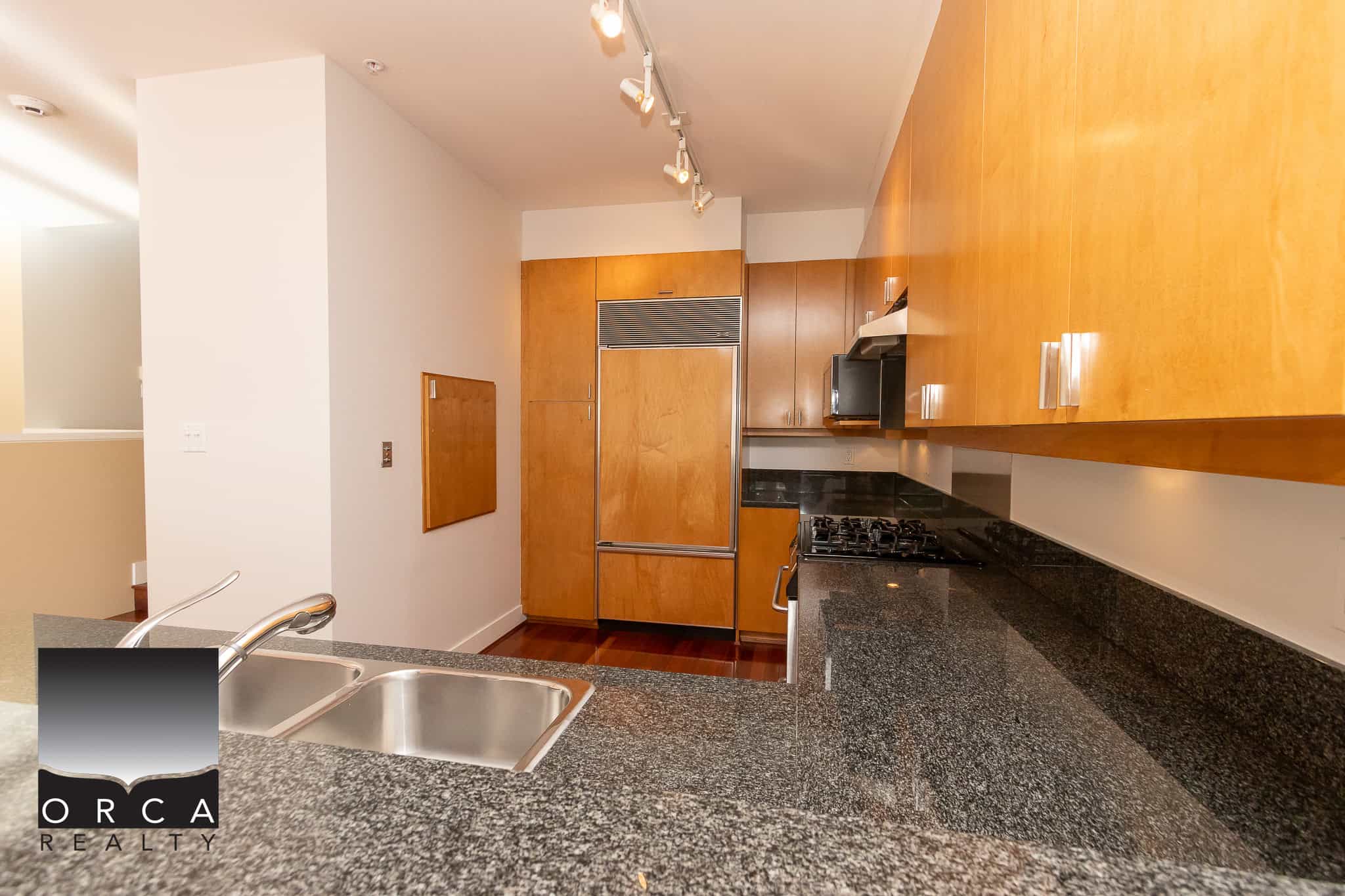 Bright modern kitchen with wooden cabinetry, black granite countertops, stainless steel appliances, and a double sink, ideal for Vancouver real estate buyers seeking stylish and functional homes.