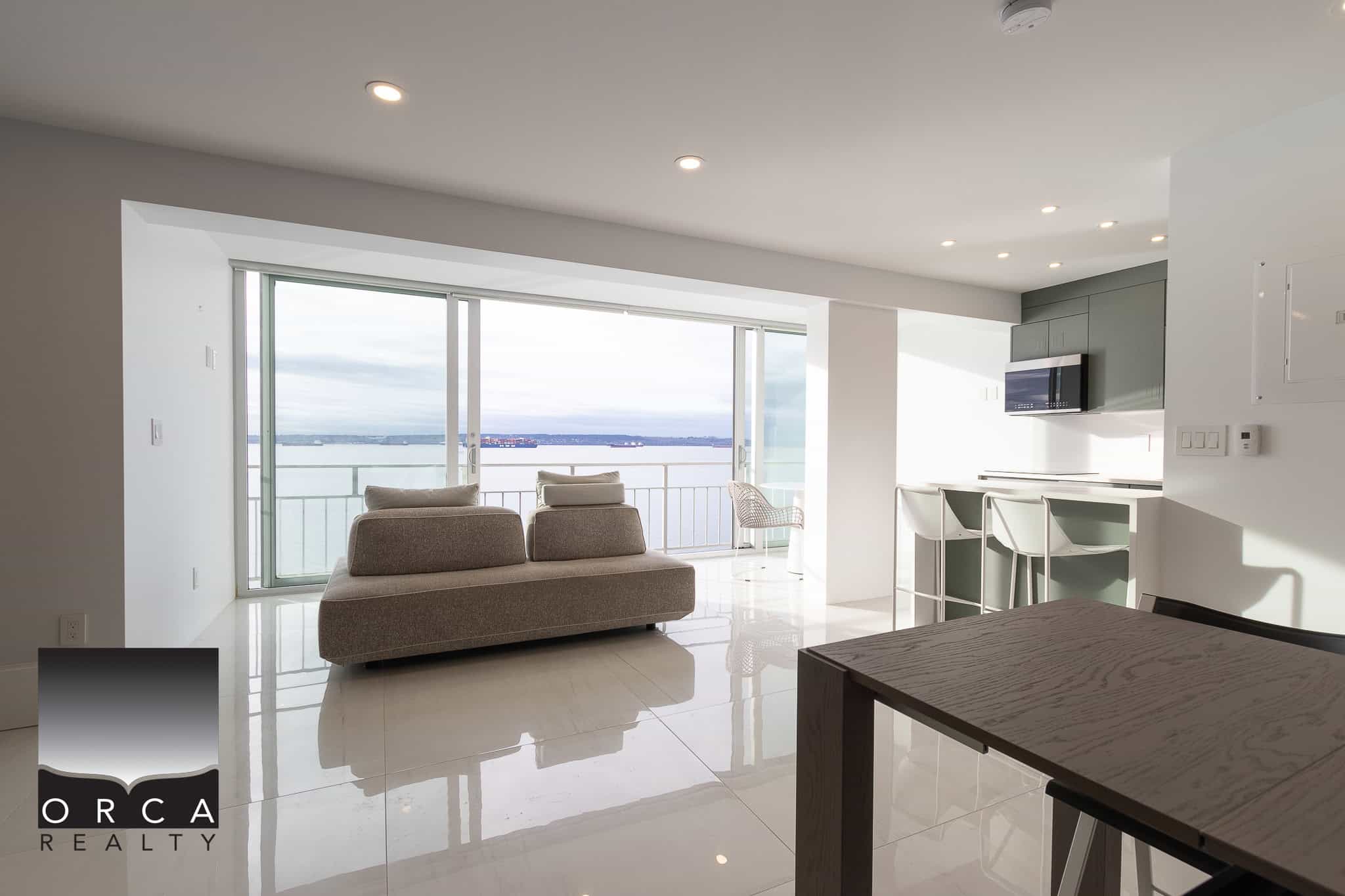 Bright modern living room with panoramic water views, sleek white interior, large sliding glass doors, and contemporary furnishings, ideal for Vancouver waterfront property.