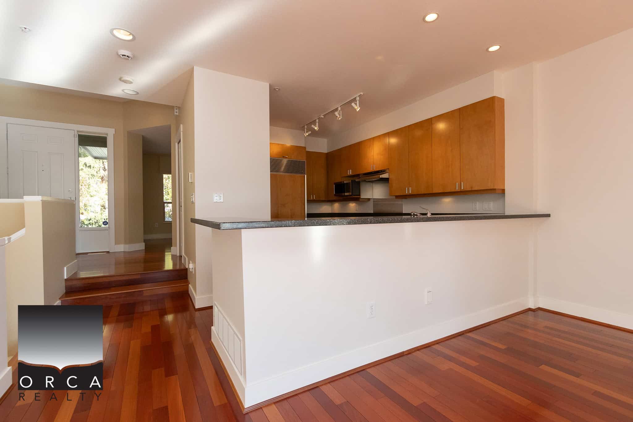 Spacious modern kitchen with warm wooden cabinets and granite countertops, open to living area, in a contemporary home listed by Orca Realty Inc.
