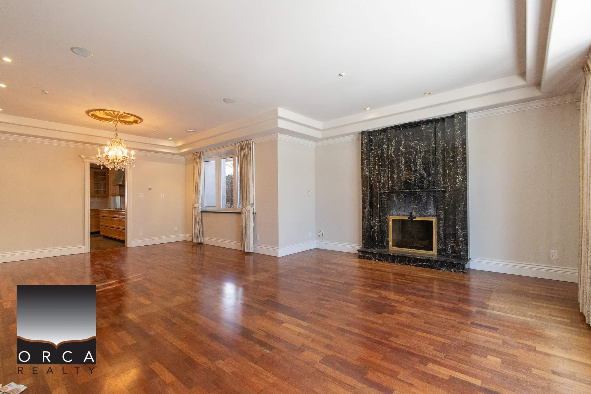 14 Spacious living room with hardwood floors, elegant fireplace, and large windows, showcasing a luxurious home interior by Orca Realty Inc. in Victoria, BC.
