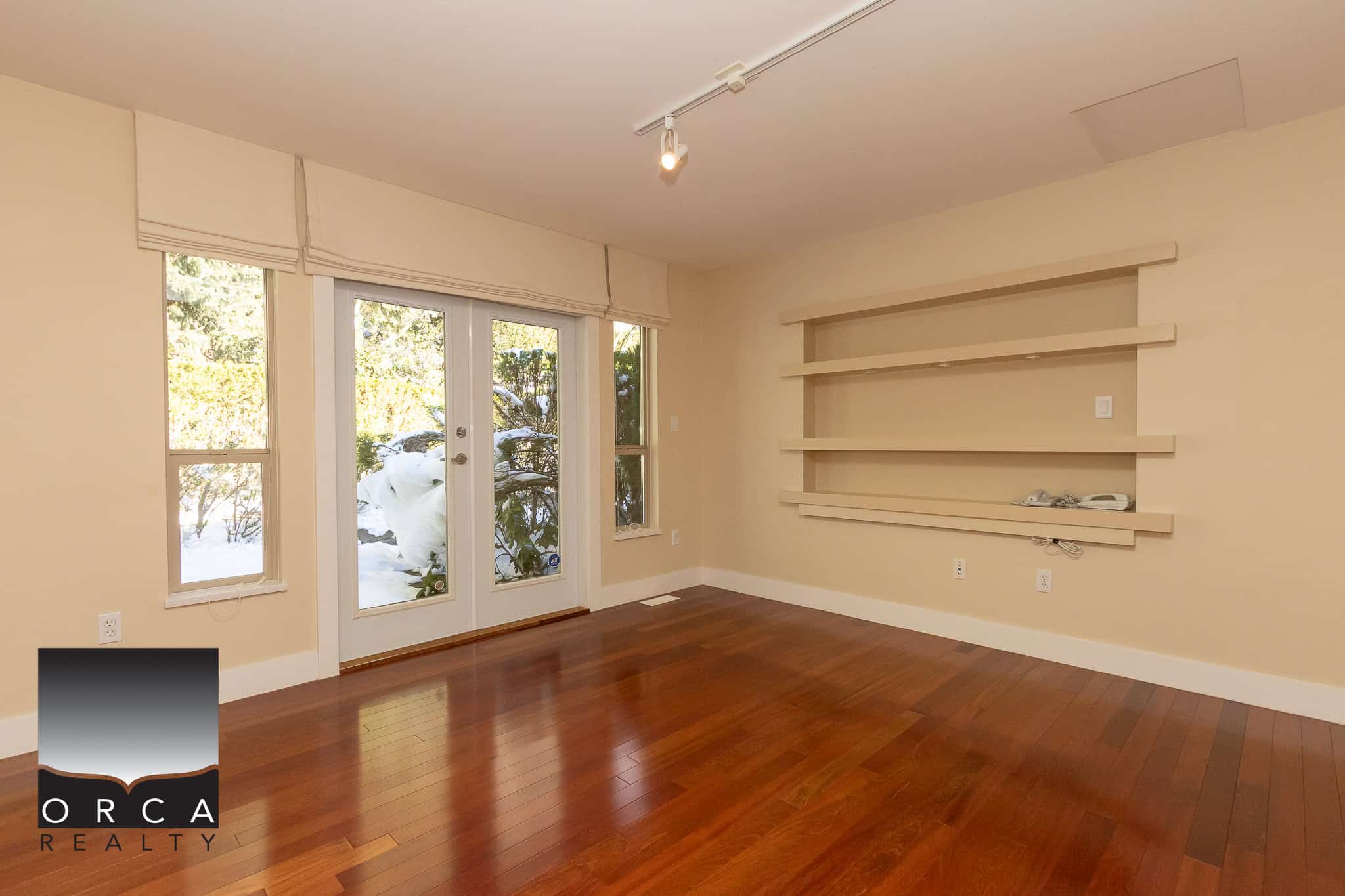 Bright and spacious living room with large windows, sliding glass door leading to the backyard, and modern built-in wall shelves, ideal for Vancouver Island residential properties.