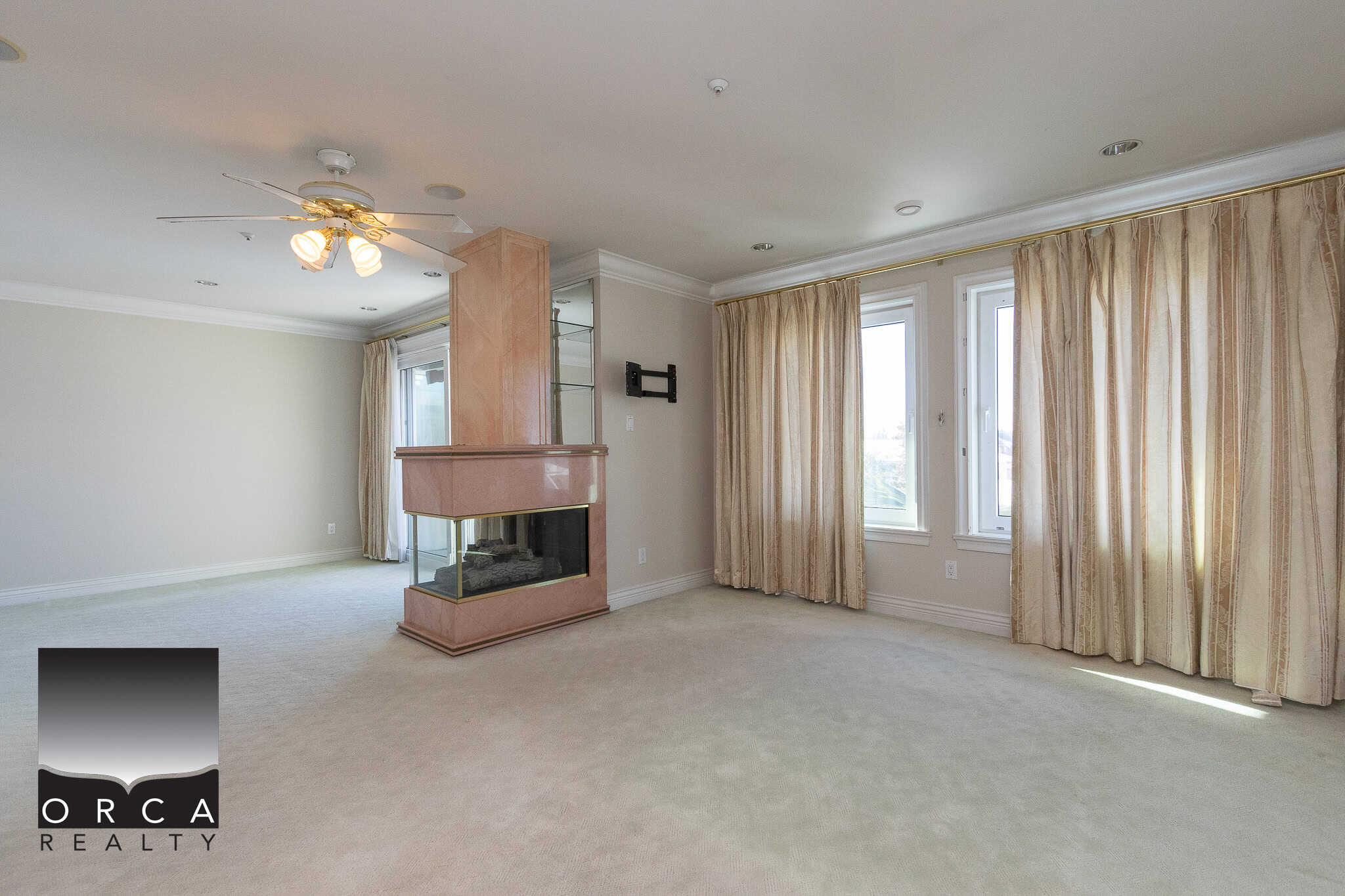 15 Bright and spacious living room in a modern home listed by Orca Realty Inc., featuring large windows, elegant curtains, a cozy fireplace, and ample natural light, ideal for comfortable family living.