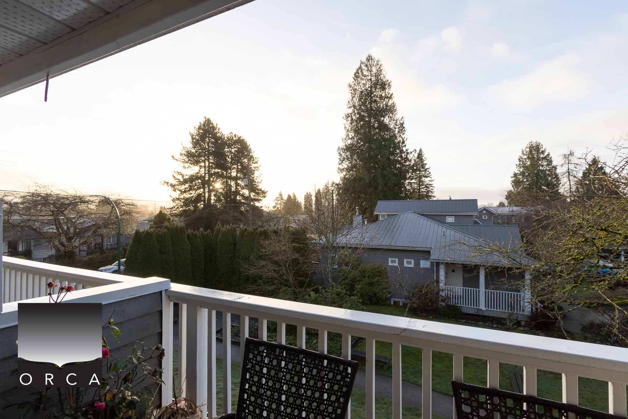 Cozy residential neighbourhood view from a balcony, featuring mature trees and charming houses, perfect for clients interested in Vancouver Island real estate and properties near outdoor amenities.