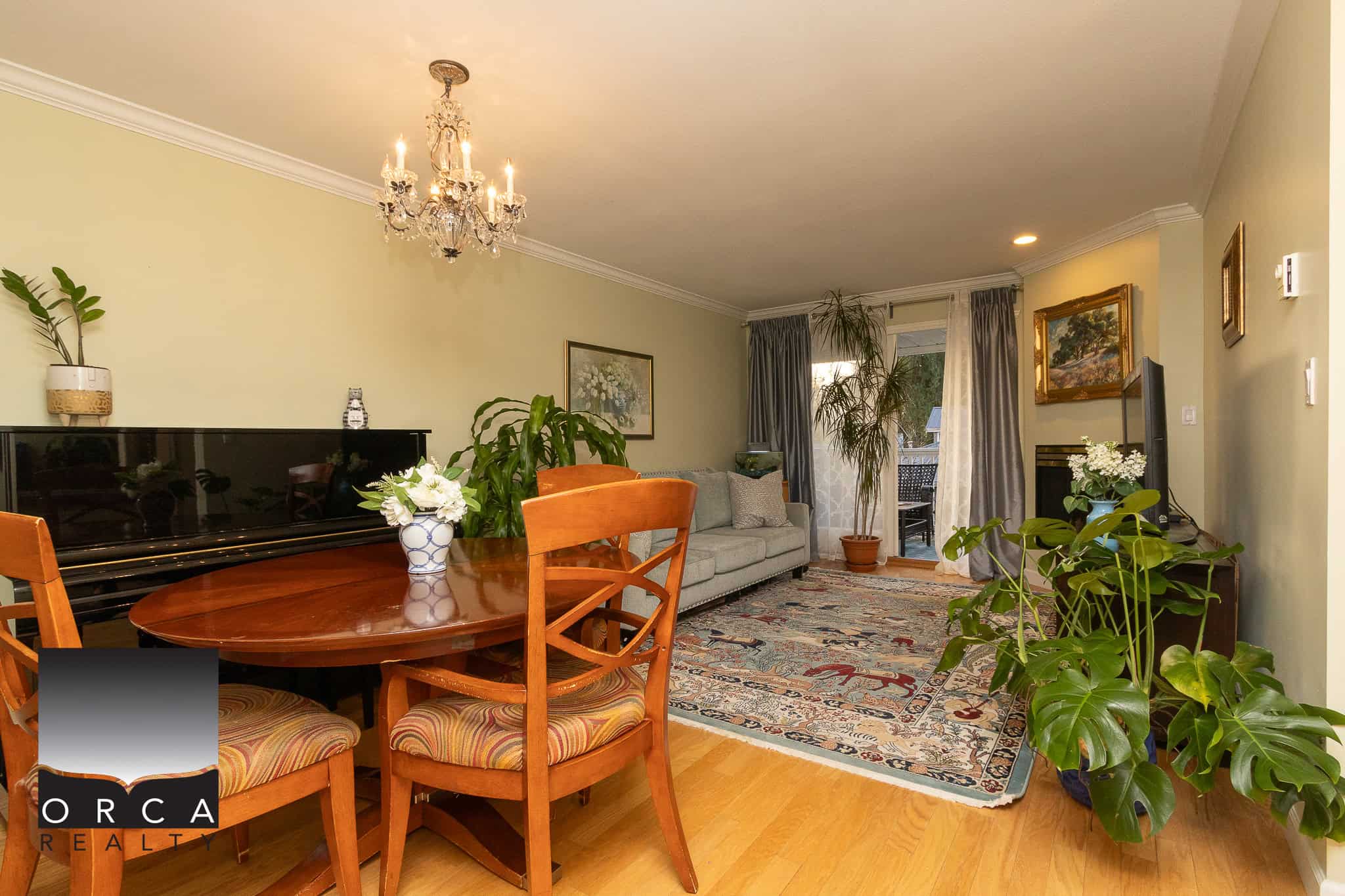 Spacious living room with elegant decor, large windows, and indoor plants, featuring a dining area, a comfortable sofa, and a balcony, perfect for seamless indoor-outdoor living in Victoria, BC.