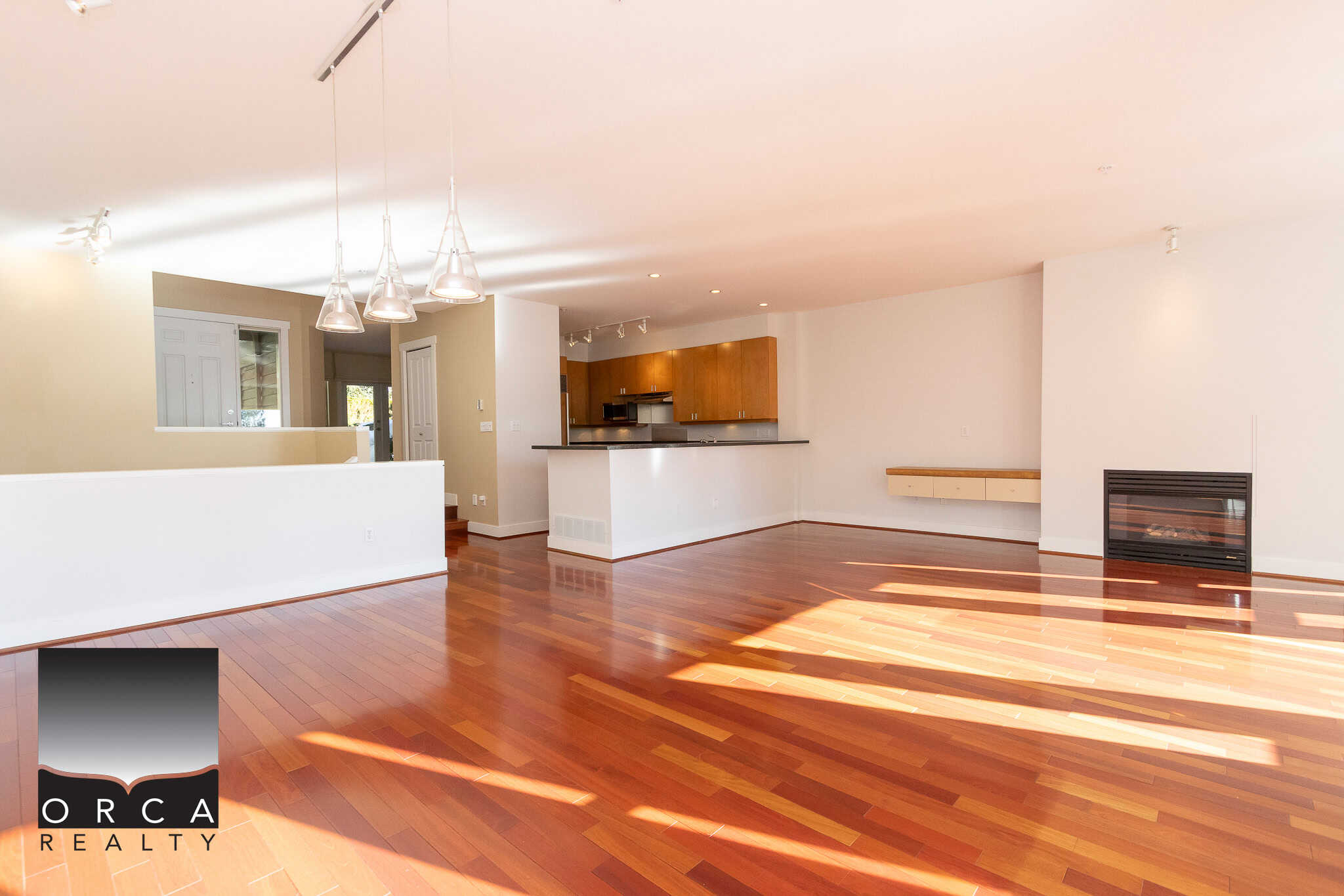 Spacious open-concept living room with hardwood floors, modern fireplace, and abundant natural light, part of a Vancouver Island home listed by Orca Realty Inc.