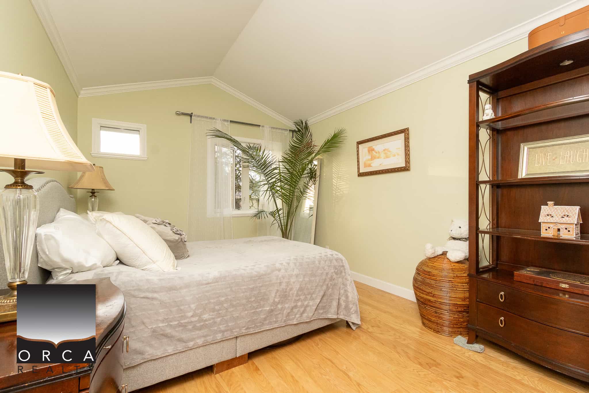 Bright and cozy bedroom with soft green walls, hardwood flooring, and natural light from a window, featuring elegant decor and a comfortable bed, ideal for a Vancouver home.