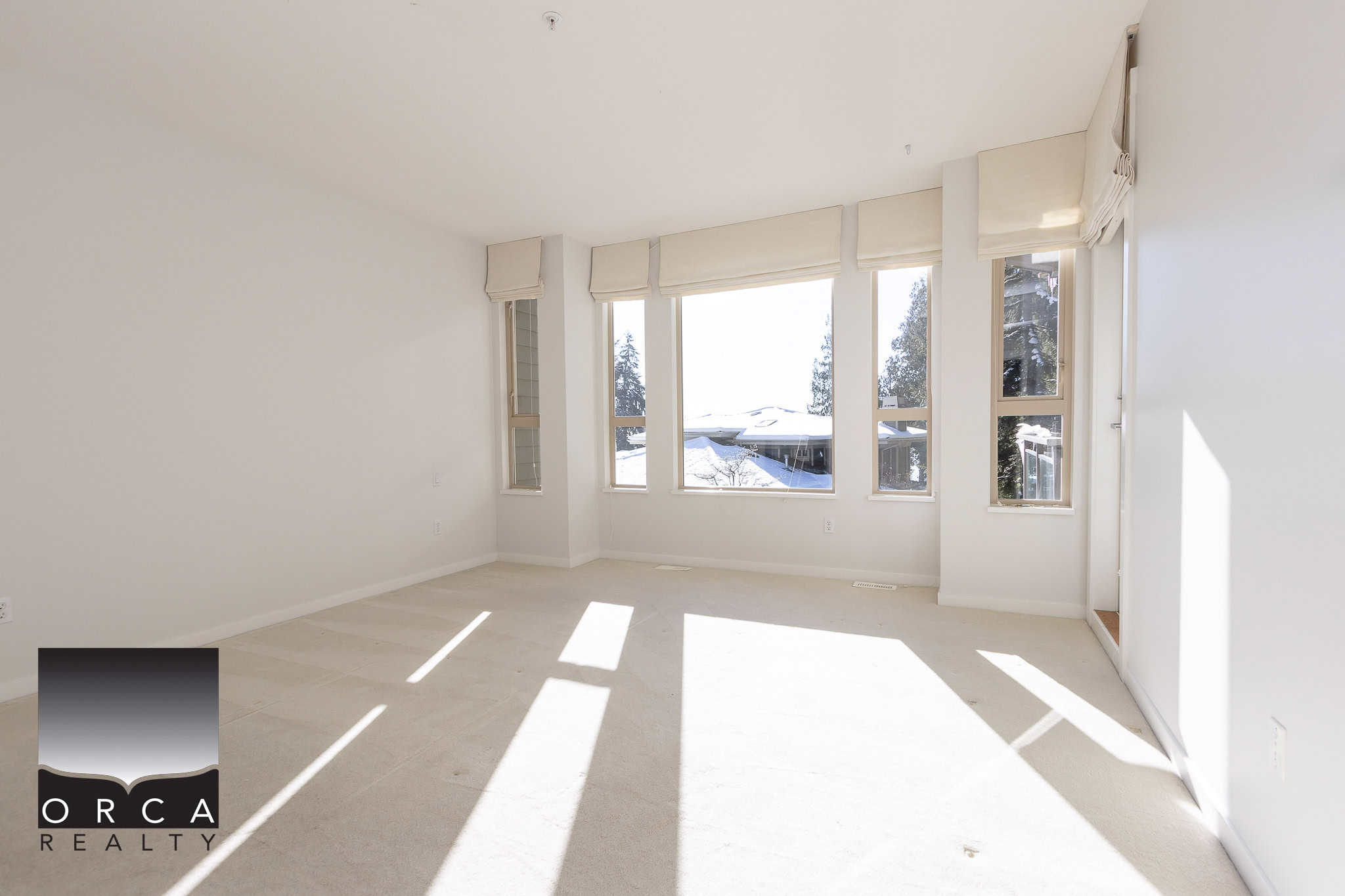 Spacious bright living room with large windows showcasing snow-covered outdoor landscape, modern white walls, and elegant window coverings. Perfect space for cozy home living.