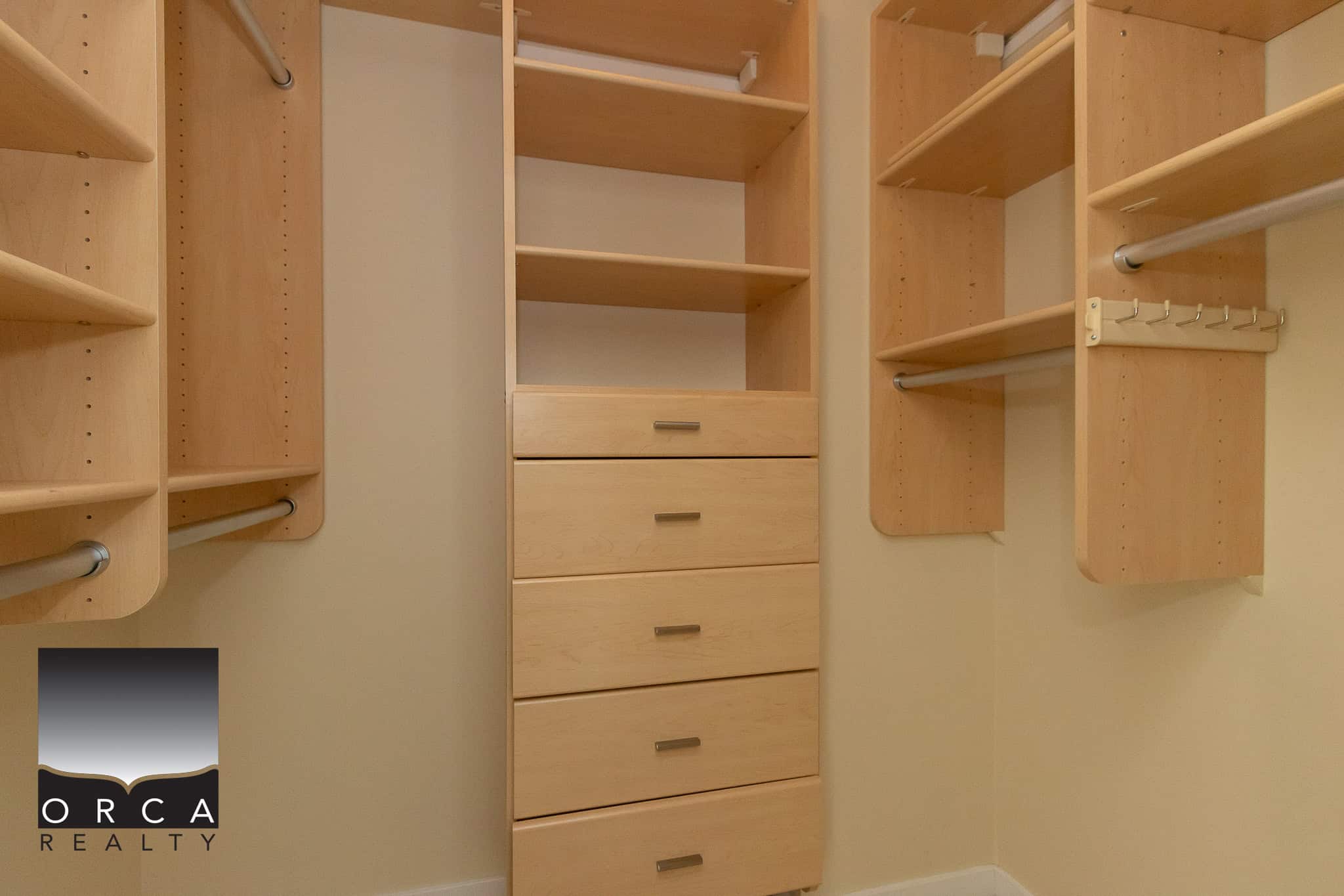 Spacious walk-in closet with built-in wooden shelves, drawers, and hanging rods for organized storage solutions. Perfect for maximizing closet space in your home or investment property.