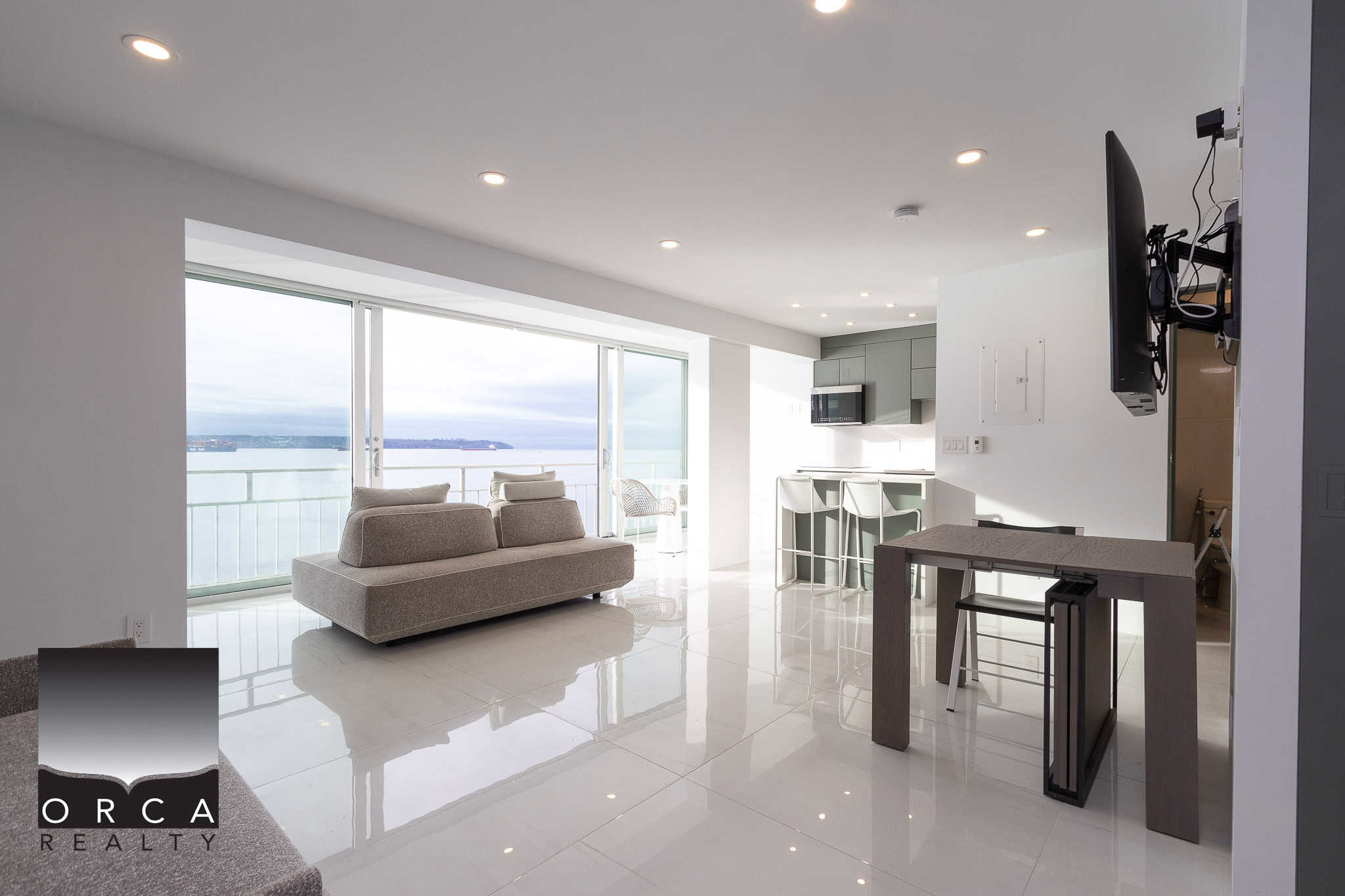 Spectacular ocean view from a modern condominium living room featuring bright natural light, sleek furnishings, and a contemporary kitchen – perfect for seaside living in Vancouver, BC.