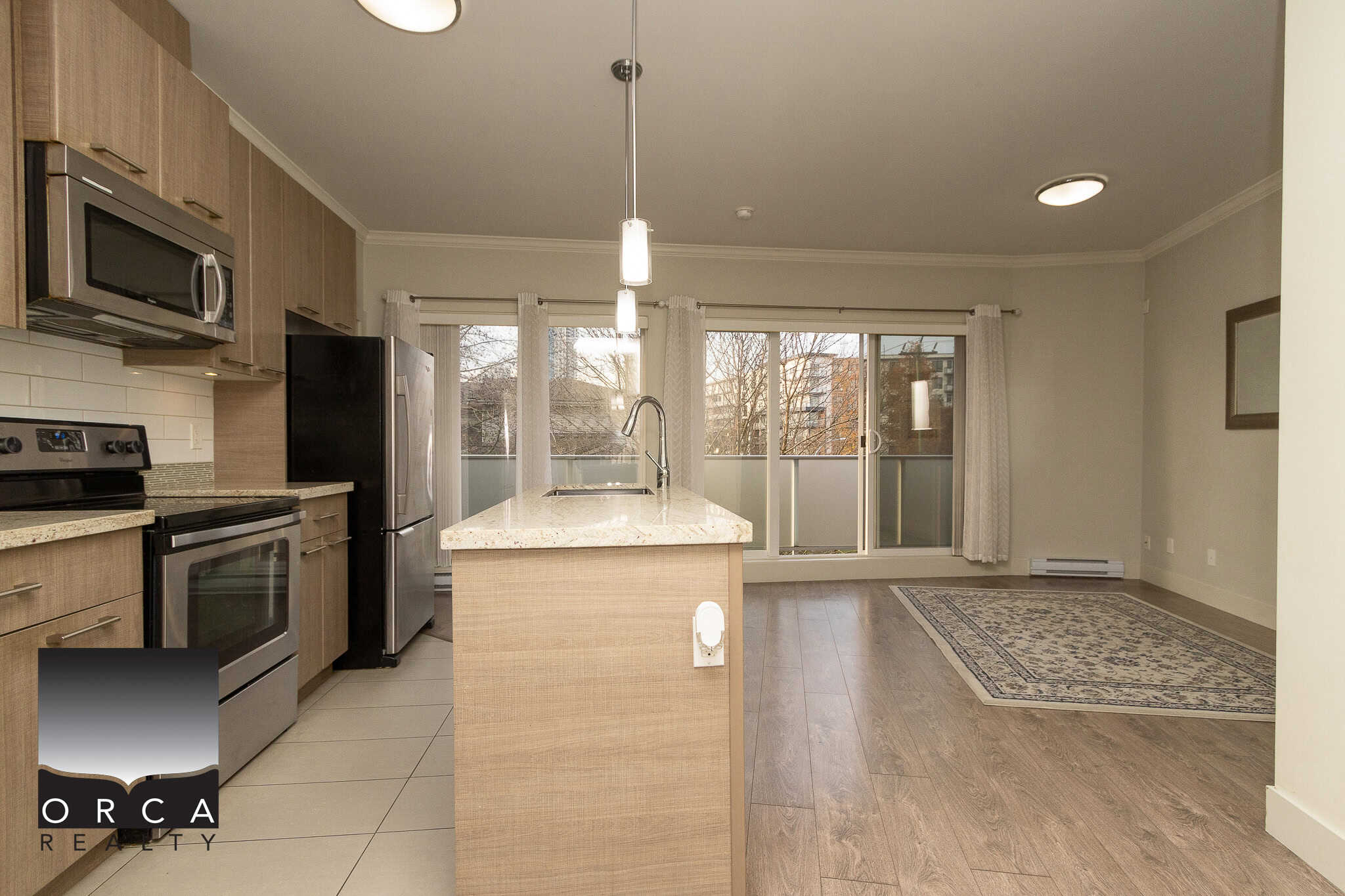 Modern kitchen with stainless steel appliances and granite countertops in a spacious Vancouver apartment, featuring an open-concept living and dining area with large windows and natural light.