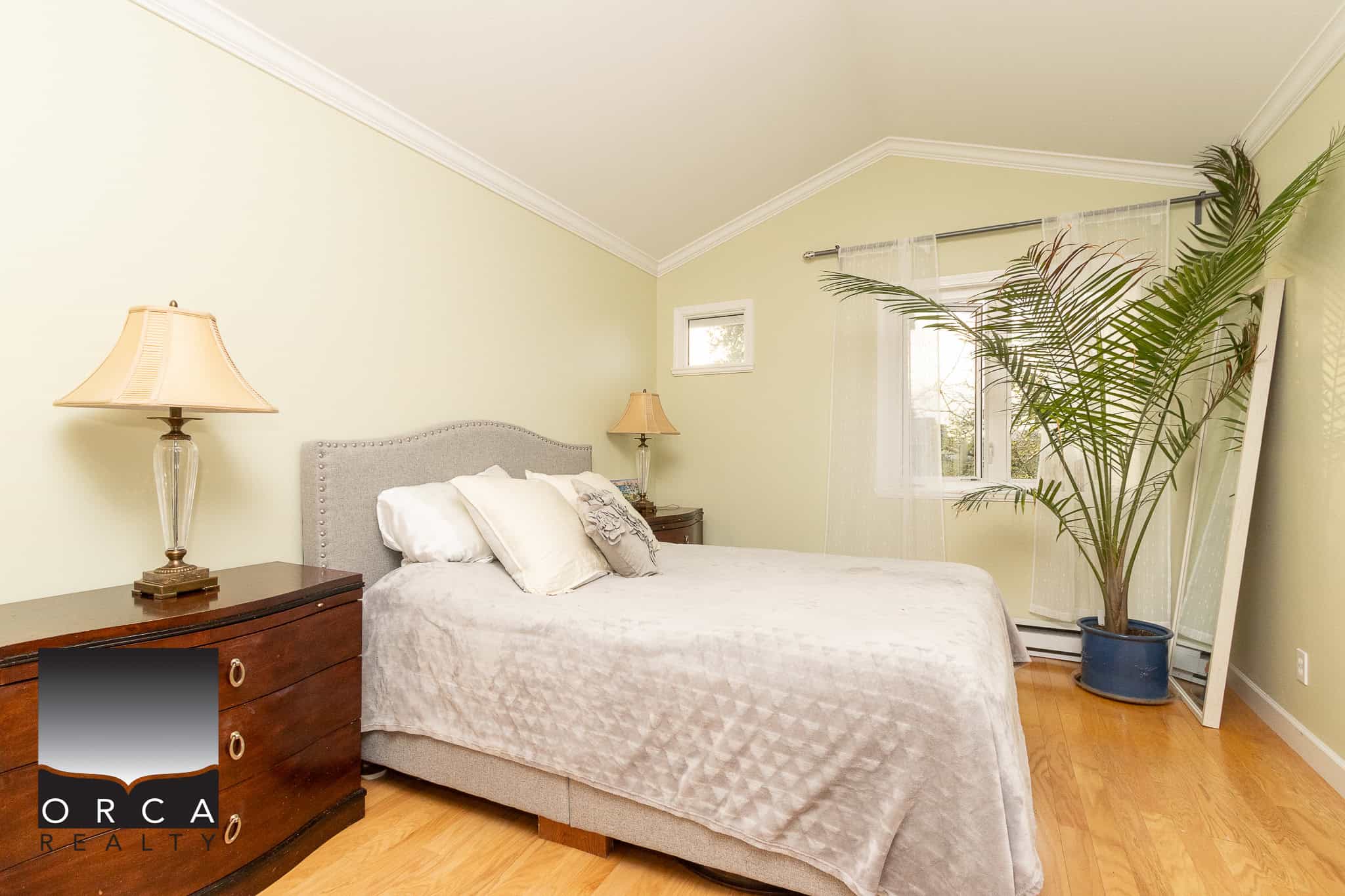 Bright bedroom with modern decor, cozy bed, wooden nightstand, elegant lamps, and natural light in a Vancouver home listed by Orca Realty Inc. for prime real estate opportunities.
