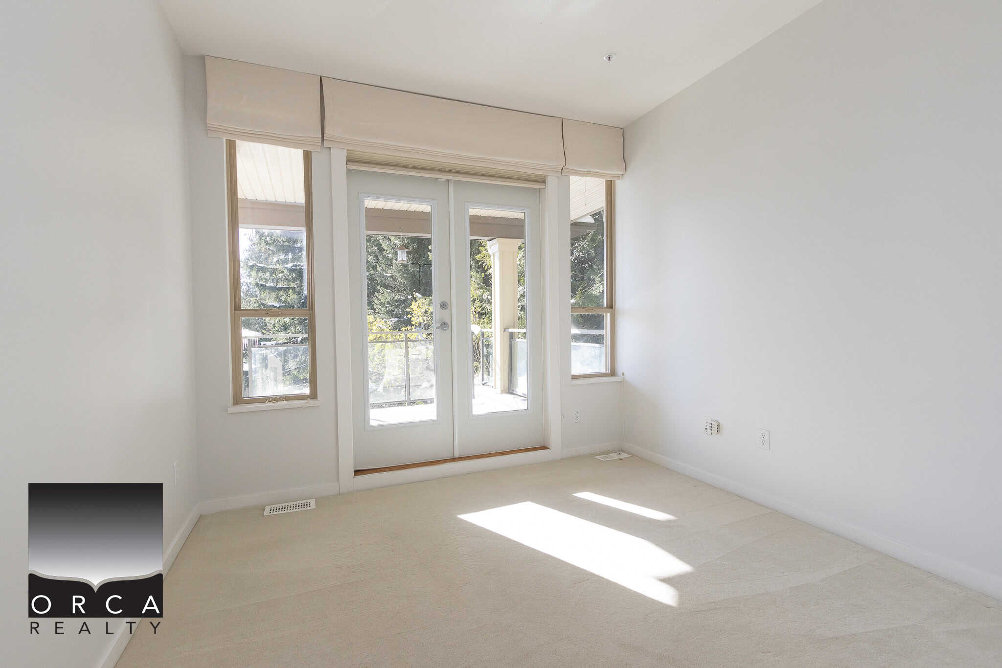 Bright empty room with large windows and glass door leading to balcony, ideal for Vancouver Island real estate listings and home staging.