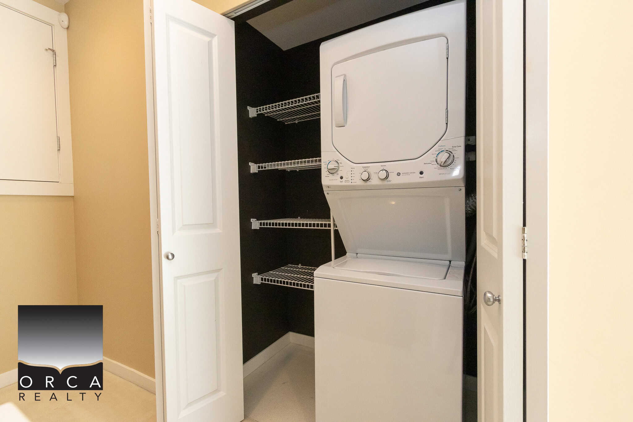 Stacked washer and dryer unit inside a closet with shelving in a modern home.