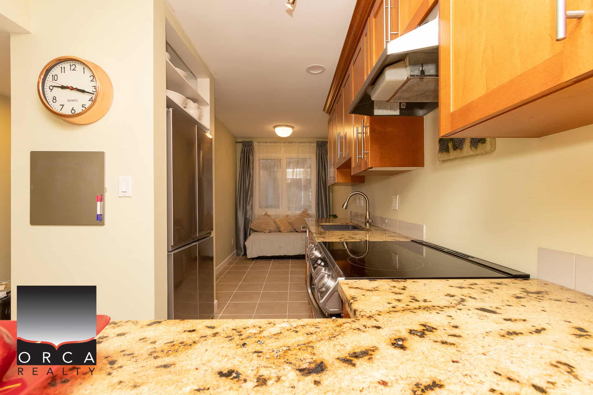 Bright modern kitchen with granite countertop, wooden cabinetry, stainless steel appliances, and cozy living space, perfect for Vancouver Island real estate investments.