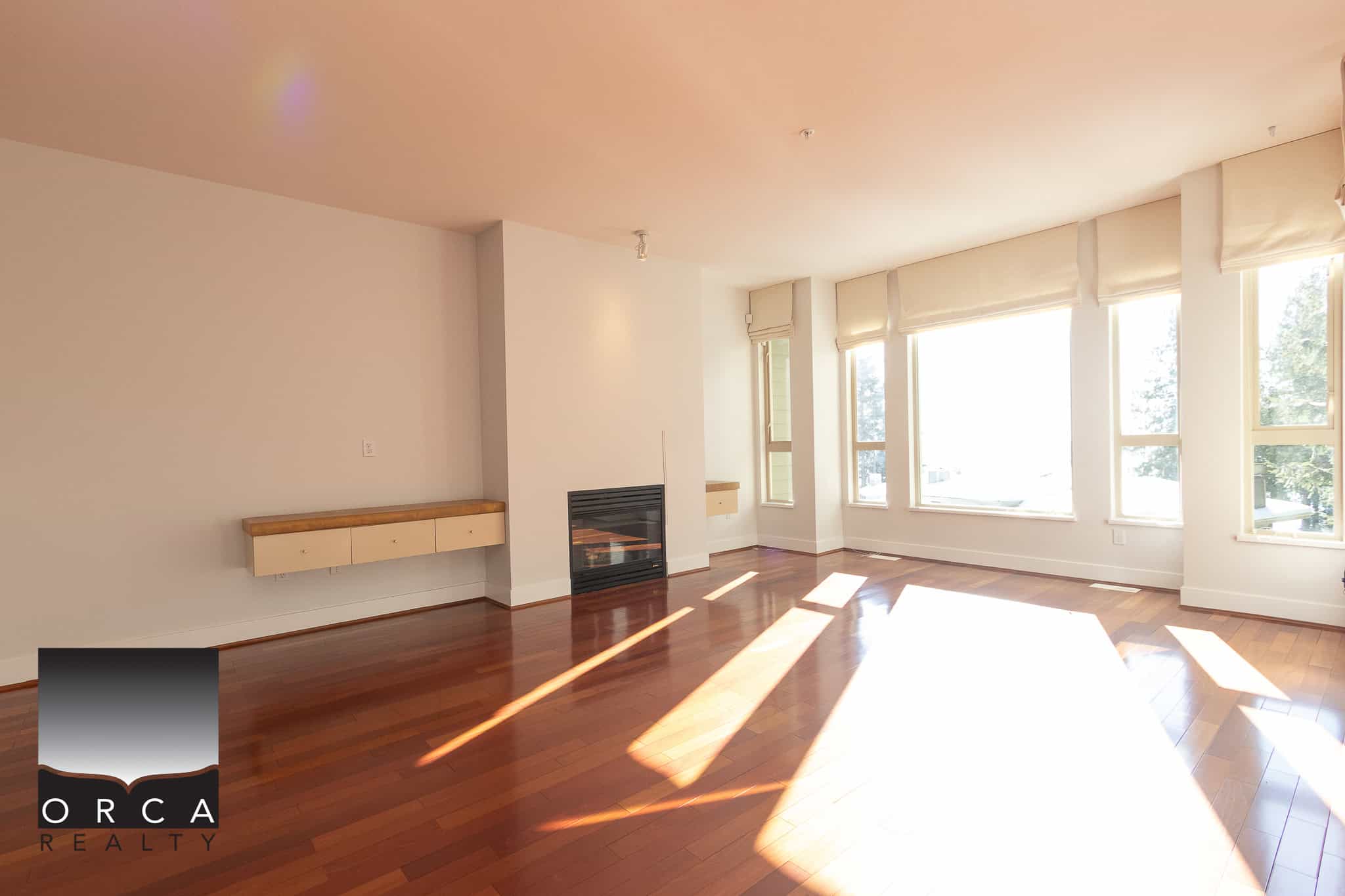 Bright spacious living room with large windows and hardwood floors, perfect for family gatherings and entertaining. Modern fireplace and natural light enhance the inviting atmosphere.