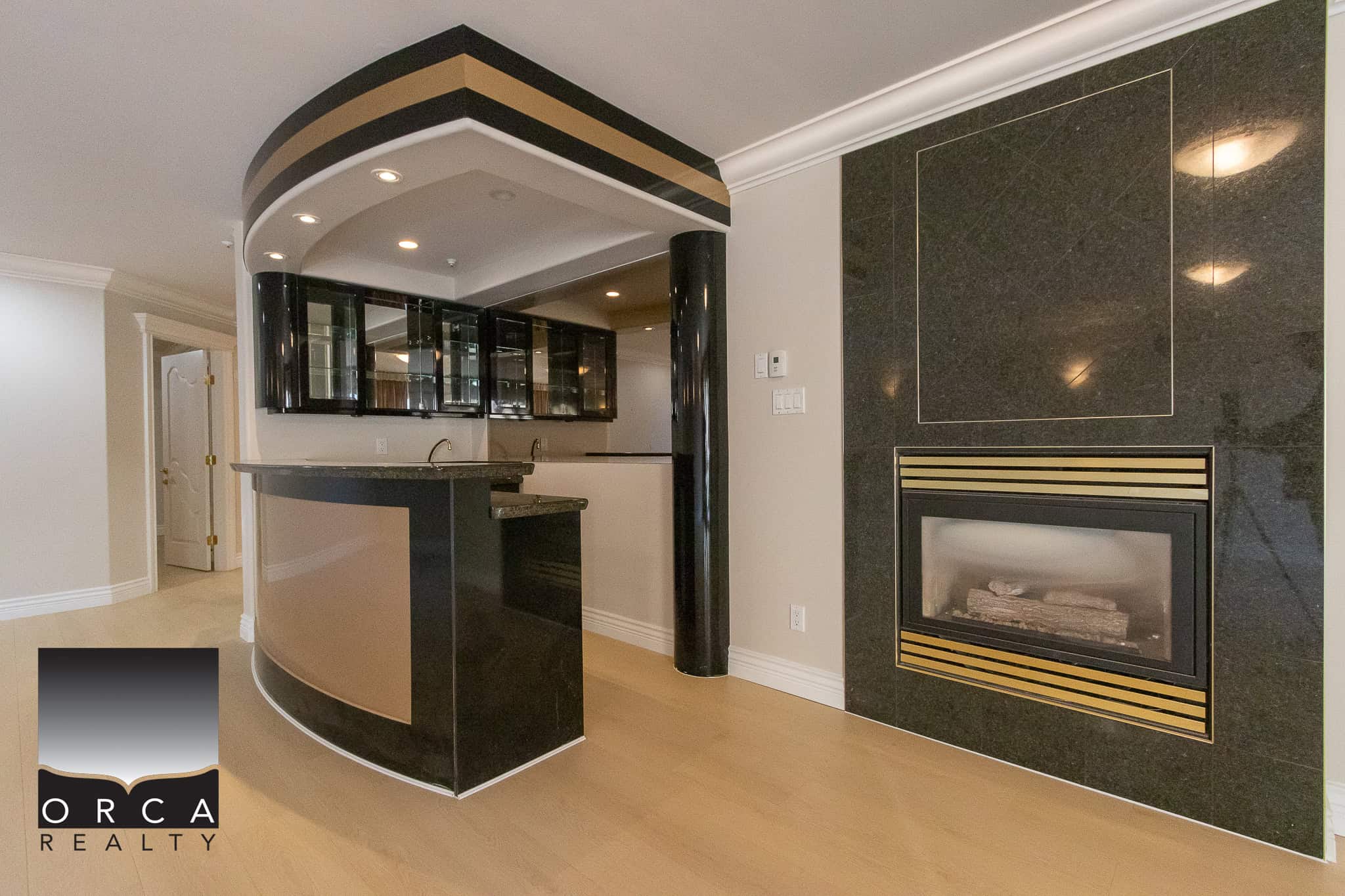 26 Luxurious living room featuring a modern black marble fireplace and a sleek black curved bar with glass cabinetry, highlighting upscale features and elegant interior design in a property listed by Orca Realty Inc.