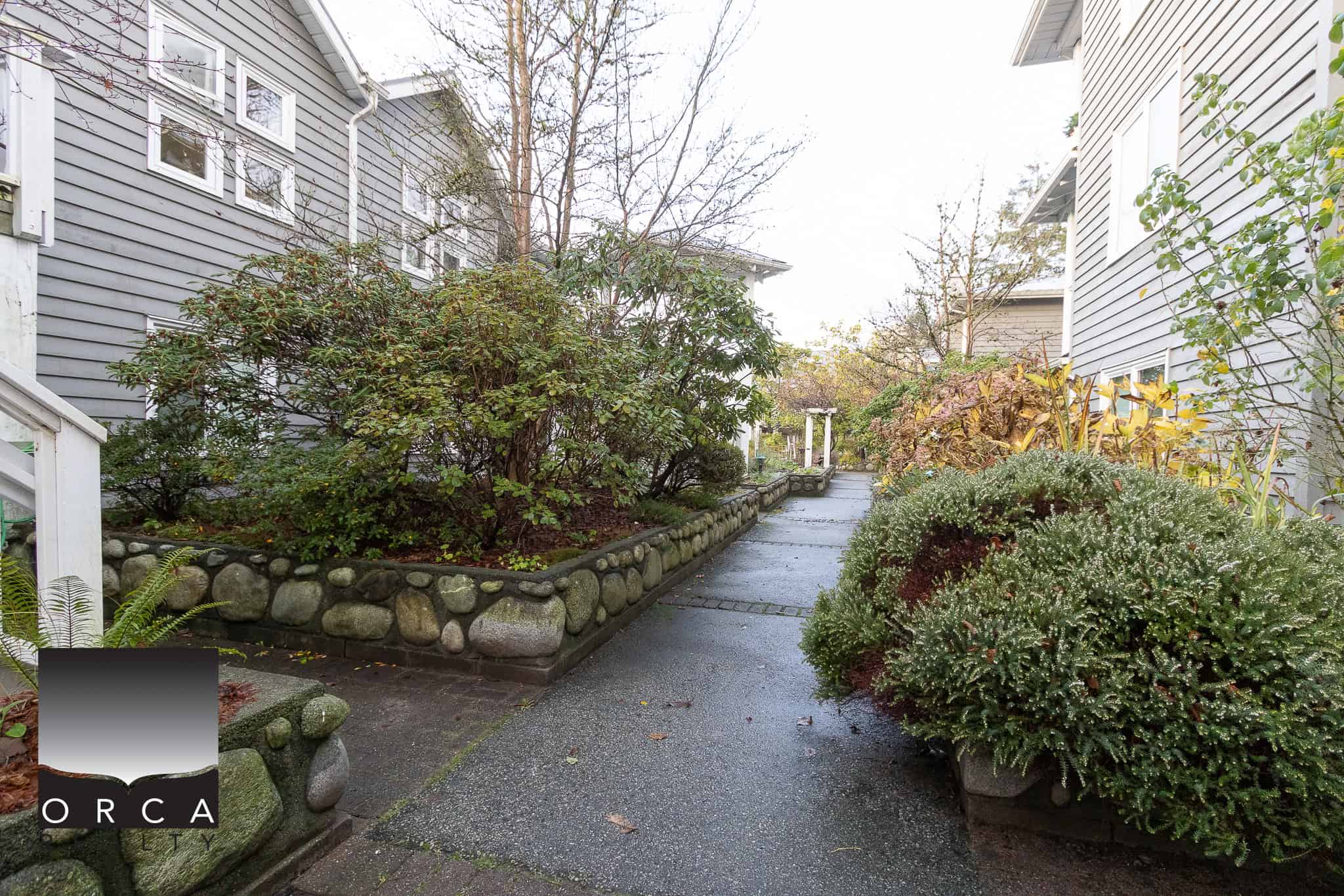 Lush garden pathway outside residential property by Orca Realty Inc., showcasing well-maintained landscaping and vibrant plants in a serene neighbourhood.