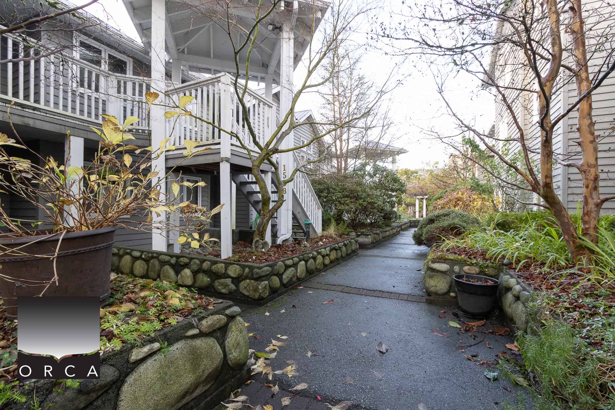 Lush residential walkway with landscaped garden beds, trees, and stone borders, showcasing the inviting outdoor space of Orca Realty Inc. properties in Vancouver.