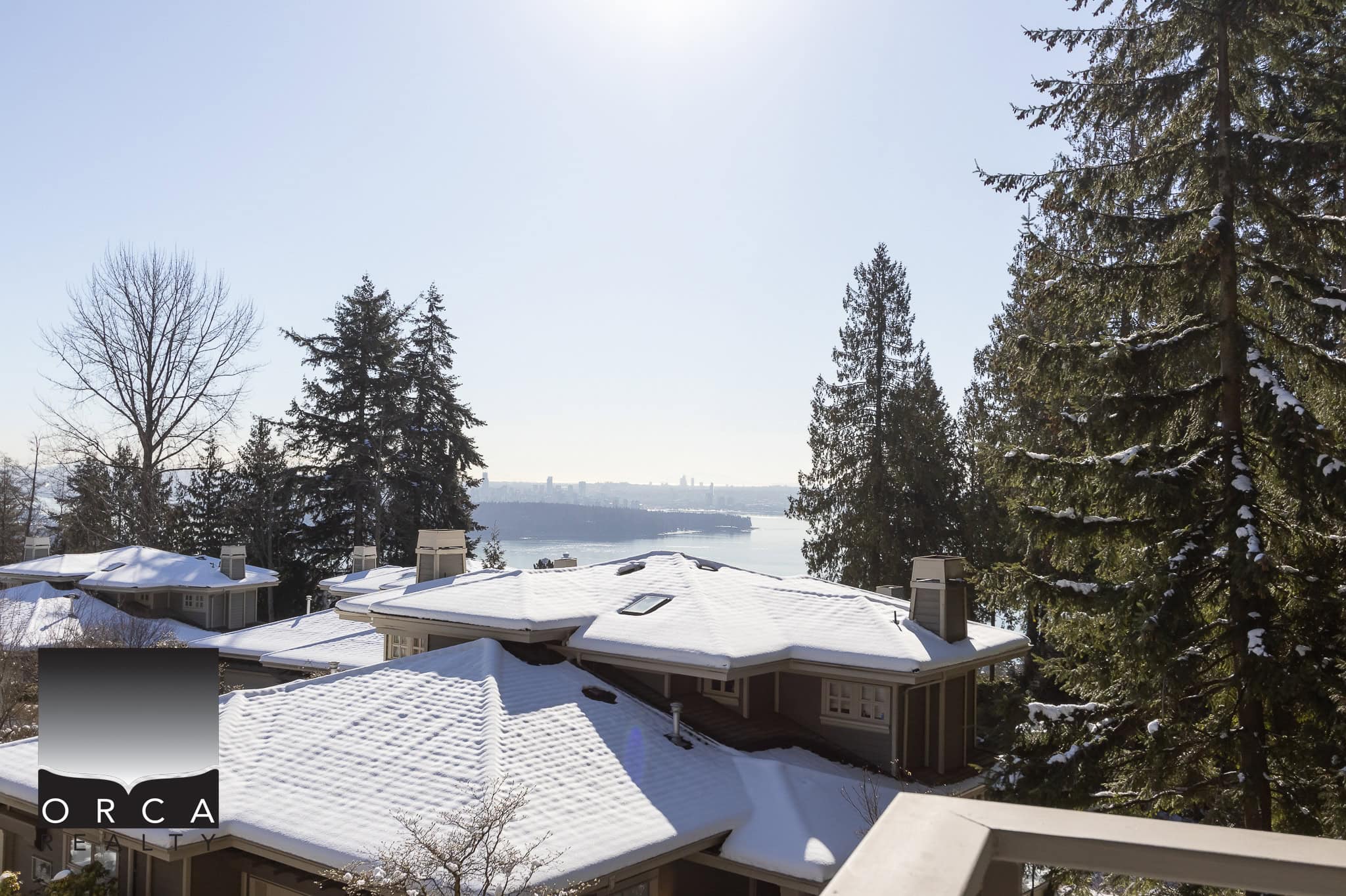 Snow-covered rooftops with a scenic water view in Vancouver, BC, showcasing prime real estate and natural beauty, perfect for potential homebuyers interested in Orca Realty Inc. listings.