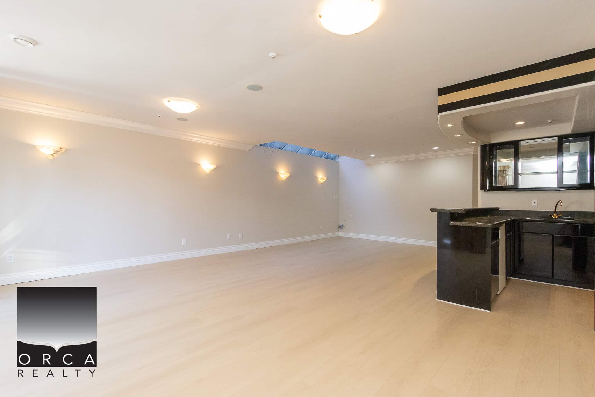 28 Spacious modern condo interior with open-plan living area, neutral walls, elegant lighting, and a sleek black kitchen featuring granite countertops and stainless steel appliances, perfect for comfortable living.