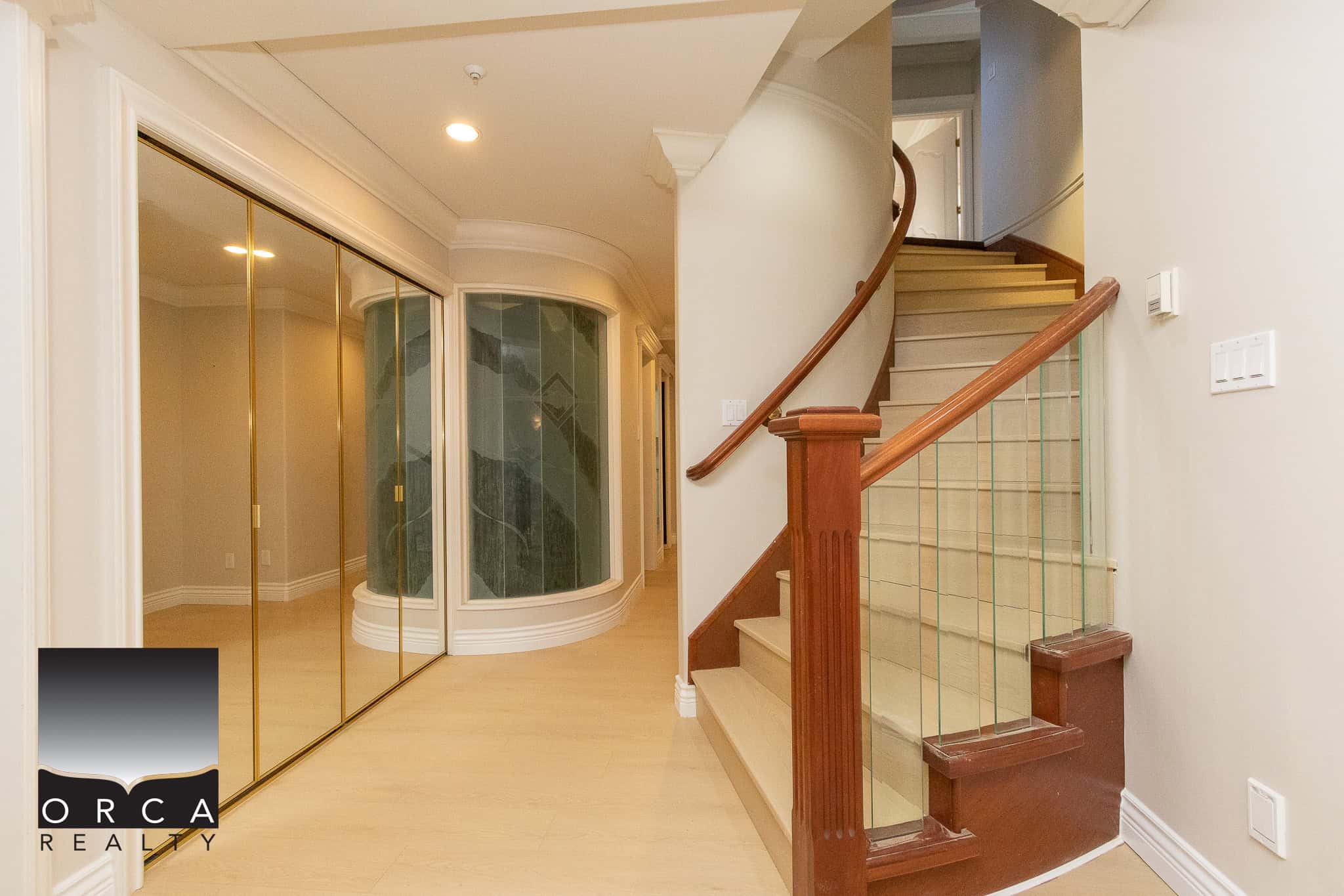 29 Spacious interior of a modern residential property featuring a curved staircase with wooden handrail and glass balusters, ample closet space with mirrored sliding doors, and neutral wall colours, showcasing quality craftsmanship by Orca Realty Inc.