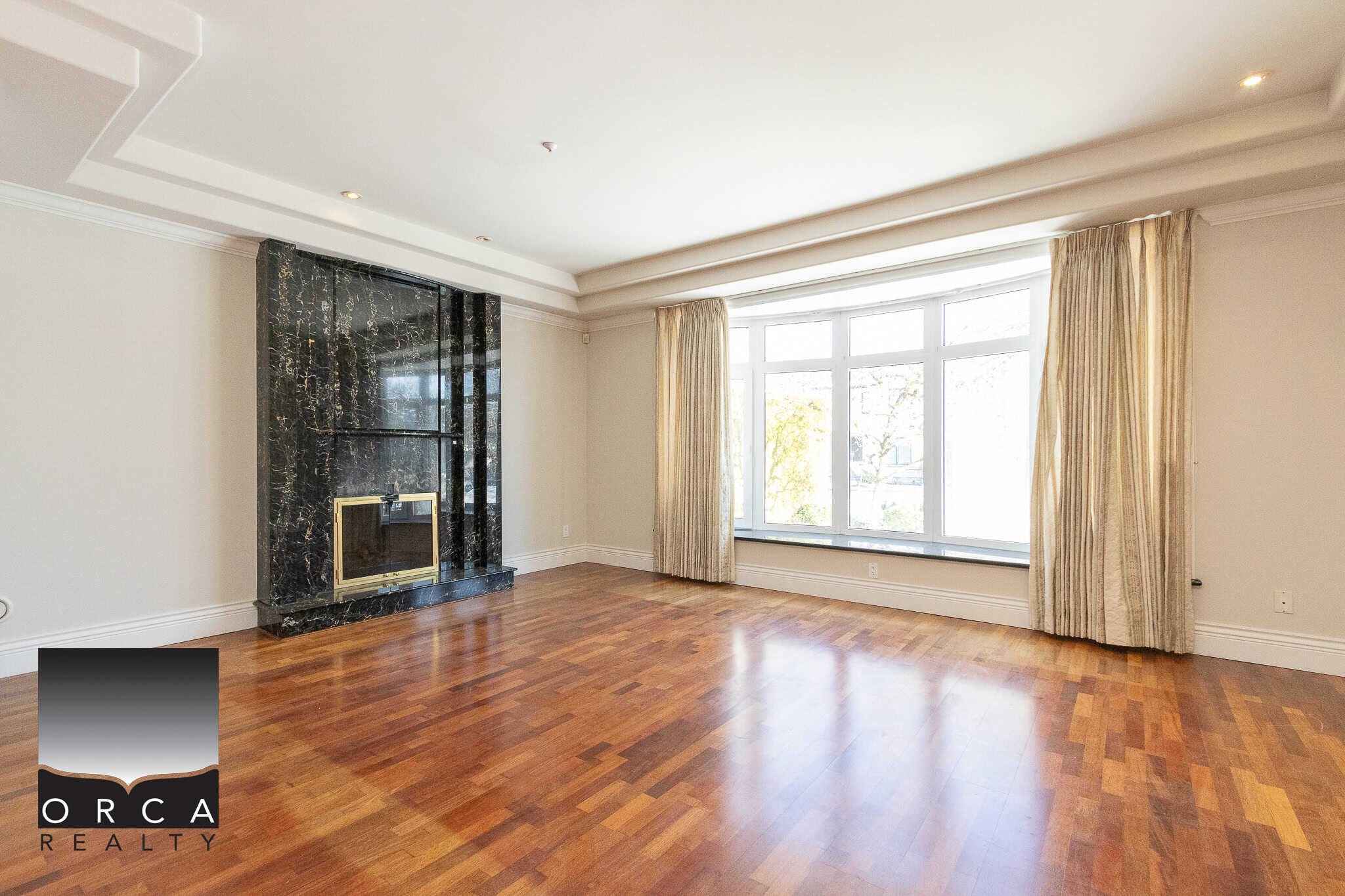 3 Spacious living room with large bay window, hardwood floors, and a modern black marble fireplace, ideal for Vancouver area real estate, showcasing elegant, bright, and comfortable home interiors.