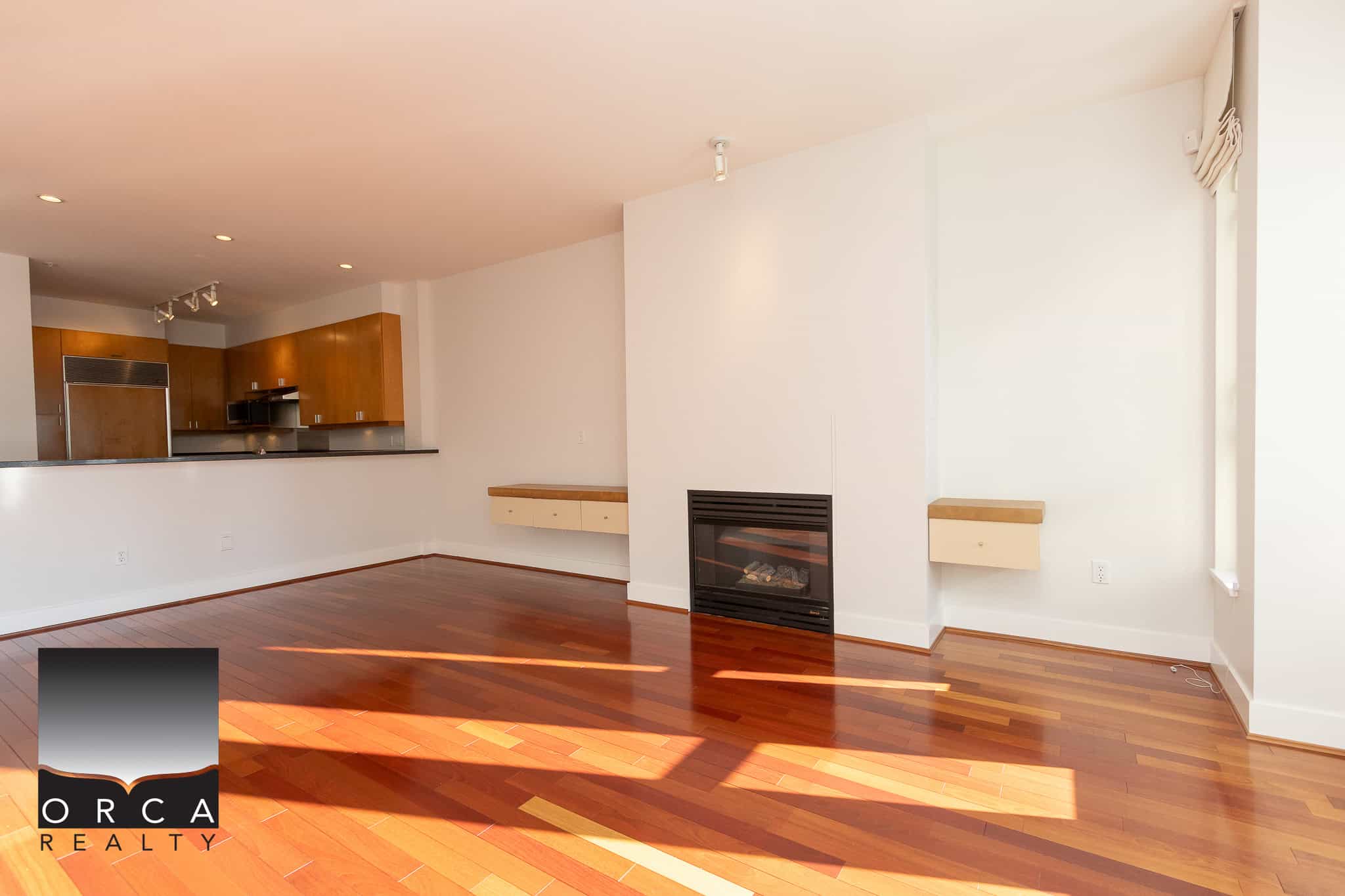 Bright spacious living room with hardwood floors, fireplace, and open-concept kitchen in a modern condo. Perfect for comfortable living and entertaining, with natural light enhancing the space.