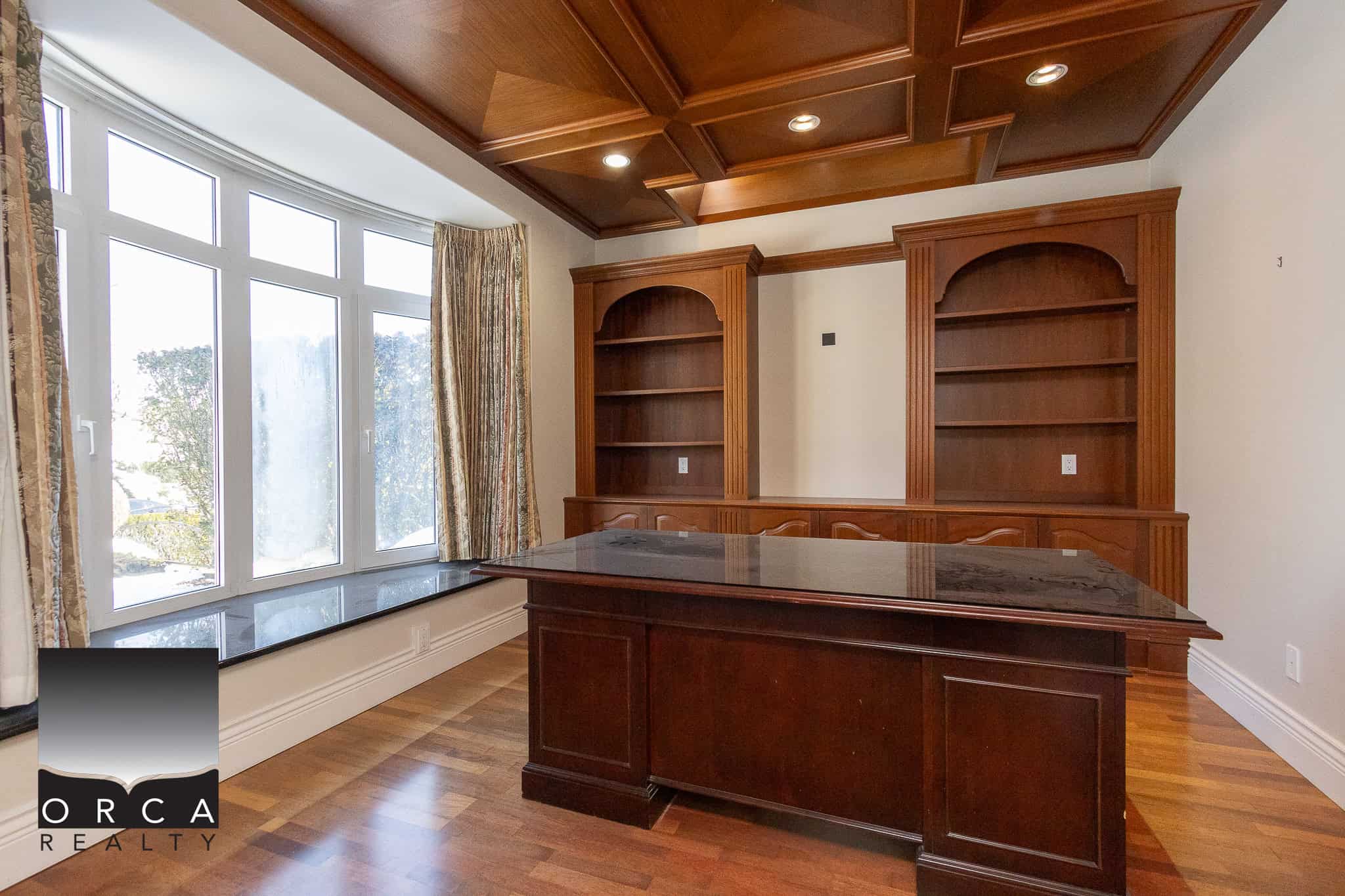 5 Dark wood home office with built-in bookshelves, large bay window with floral curtains, hardwood flooring, and a rich wood ceiling, perfect for residential or commercial real estate listings.