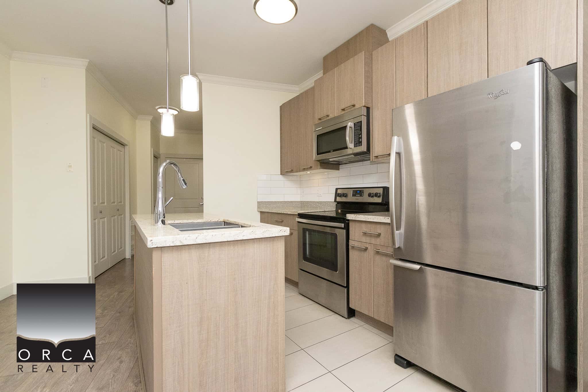 Contemporary kitchen with stainless steel appliances, wooden cabinetry, and a marble countertop island, ideal for modern Vancouver Island living and real estate investments.
