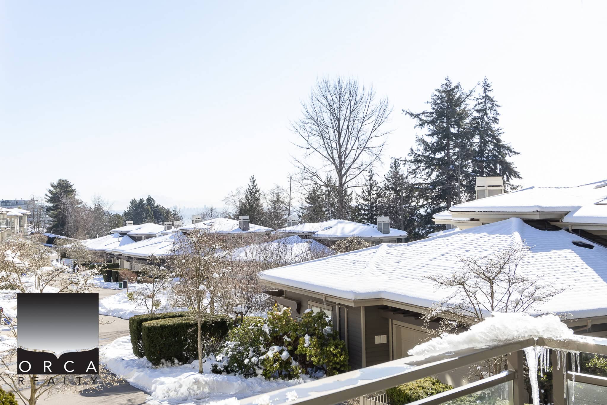 Cozy snow-covered residential neighborhood with modern houses, evergreen trees, and winter landscape, showcasing Orca Realty Inc.'s expertise in Vancouver Island real estate markets.