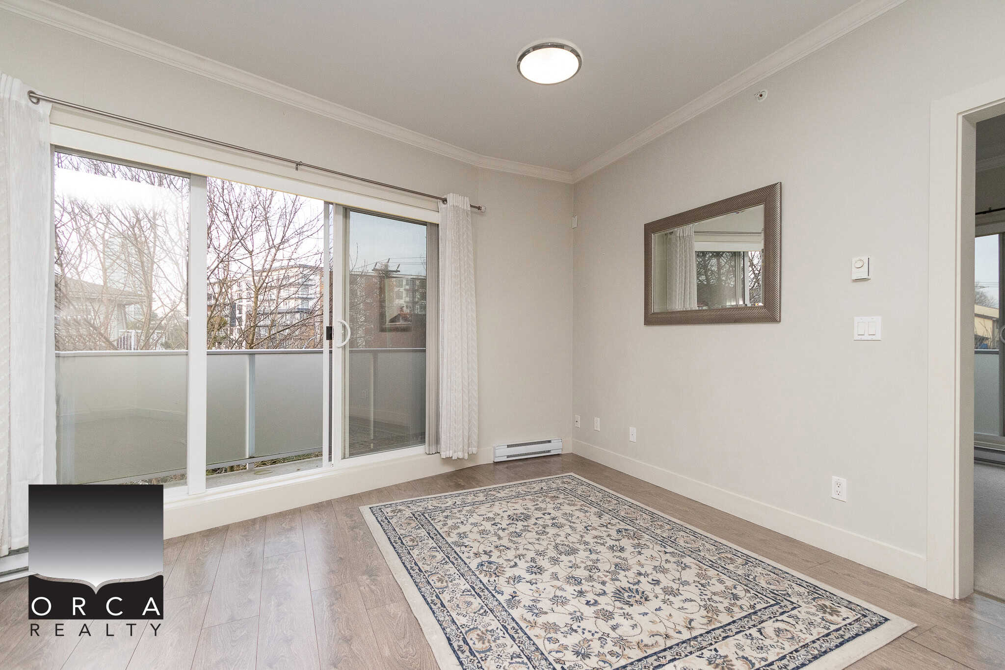 Bright living room with large sliding glass door leading to balcony, hardwood flooring, and neutral wall colors, ideal for Vancouver Island real estate options.