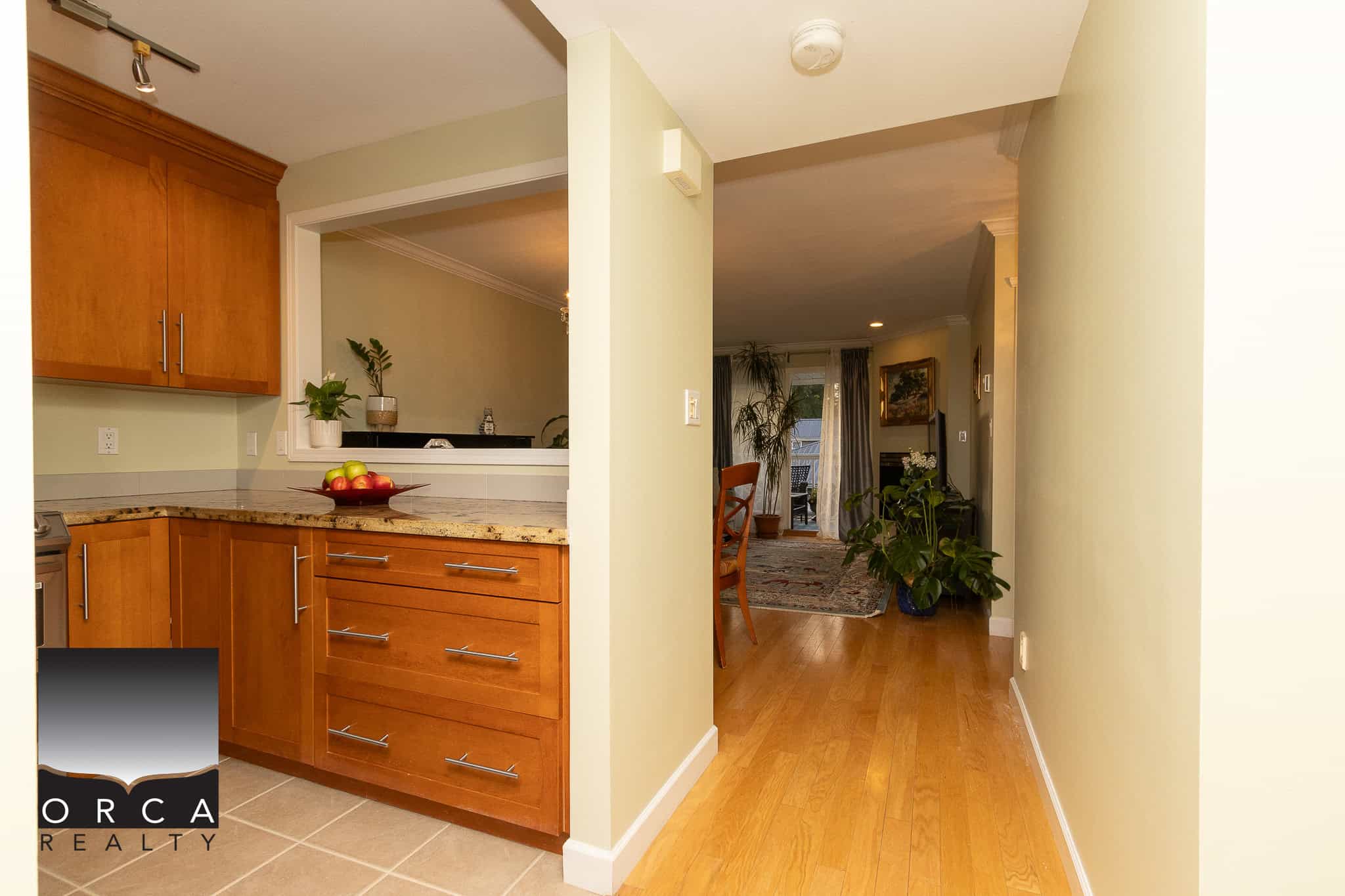 Bright open-concept kitchen and living room in a Vancouver home, featuring warm hardwood floors, modern kitchen cabinetry, and lush indoor plants, ideal for family living and entertaining.