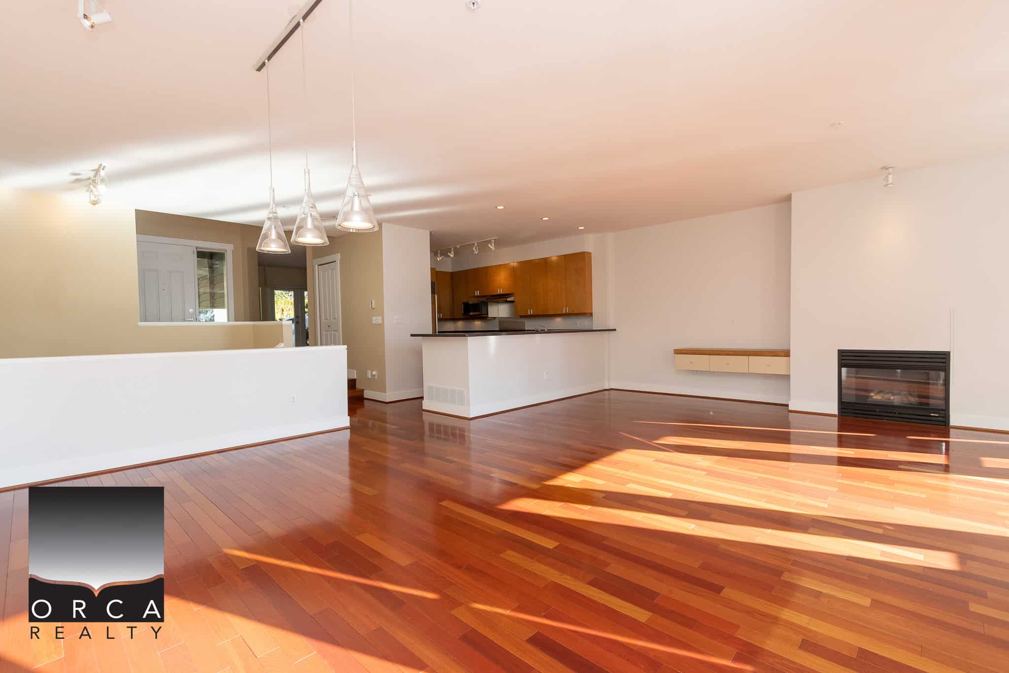 Bright spacious open-concept living room with hardwood floors, modern fireplace, and large windows in a contemporary home listed by Orca Realty Inc.