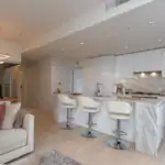 Elegant modern kitchen with white cabinetry, marble accents, and a stylish island featuring three white barstools, perfect for Vancouver-area luxury home living.