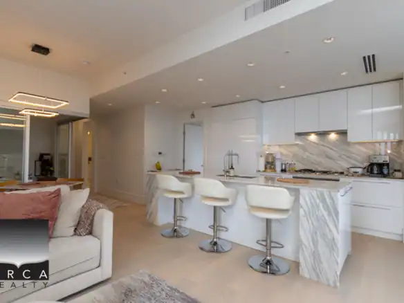 Elegant modern kitchen with white cabinetry, marble accents, and a stylish island featuring three white barstools, perfect for Vancouver-area luxury home living.