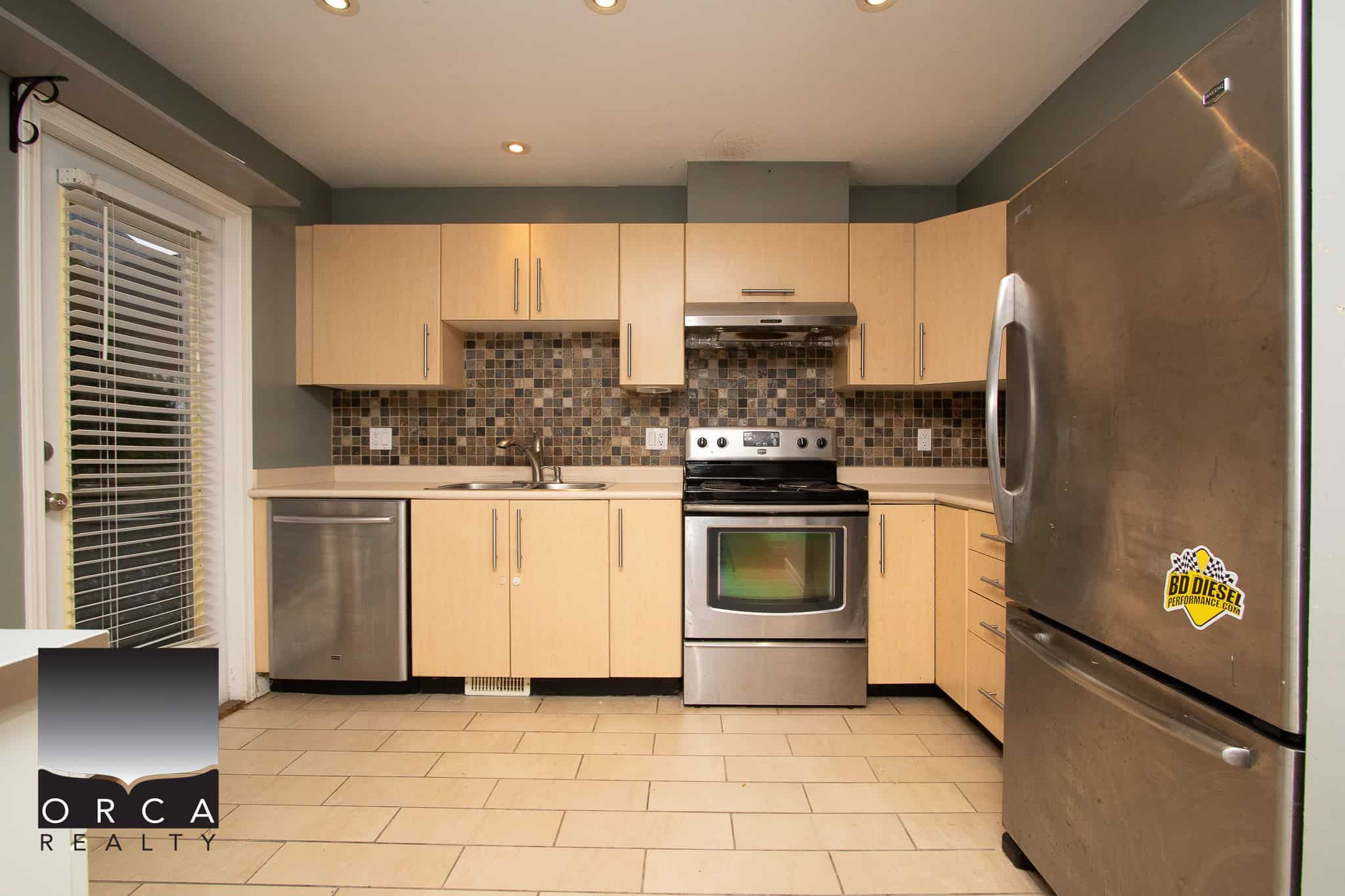 Bright modern kitchen with stainless steel appliances, beige cabinetry, tiled backsplash, and a sliding glass door leading to the backyard - ideal for Vancouver Island real estate.