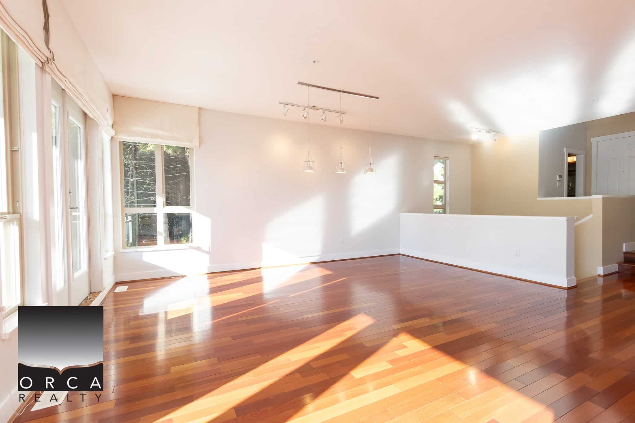 Bright open living space with hardwood floors, large windows, and modern lighting, ideal for family living and entertaining in a beautiful home listed by Orca Realty Inc.