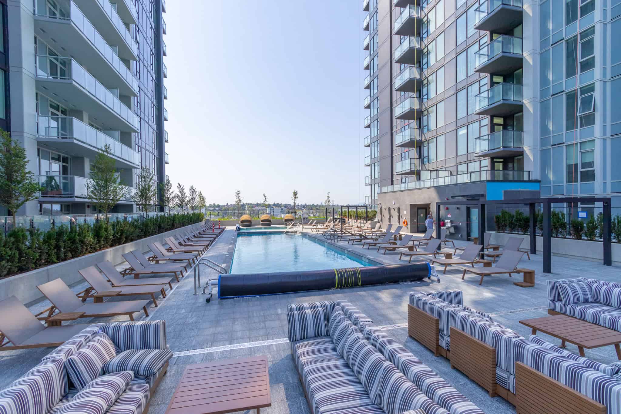 Luxurious outdoor pool area at a modern high-rise apartment building in Vancouver, featuring sun loungers, striped cushioned seating, and city views.