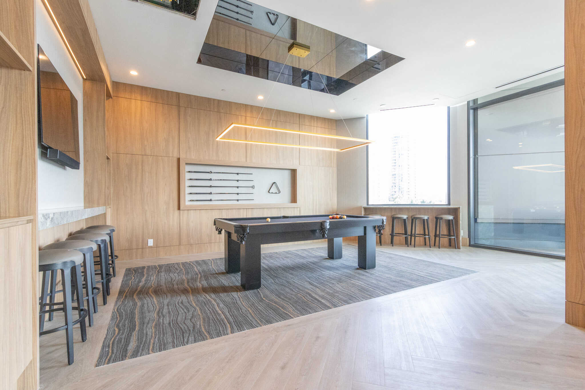 Contemporary indoor recreational lounge with pool table, modern lighting, bar stools, and large windows providing city views, ideal for community gatherings and entertainment.